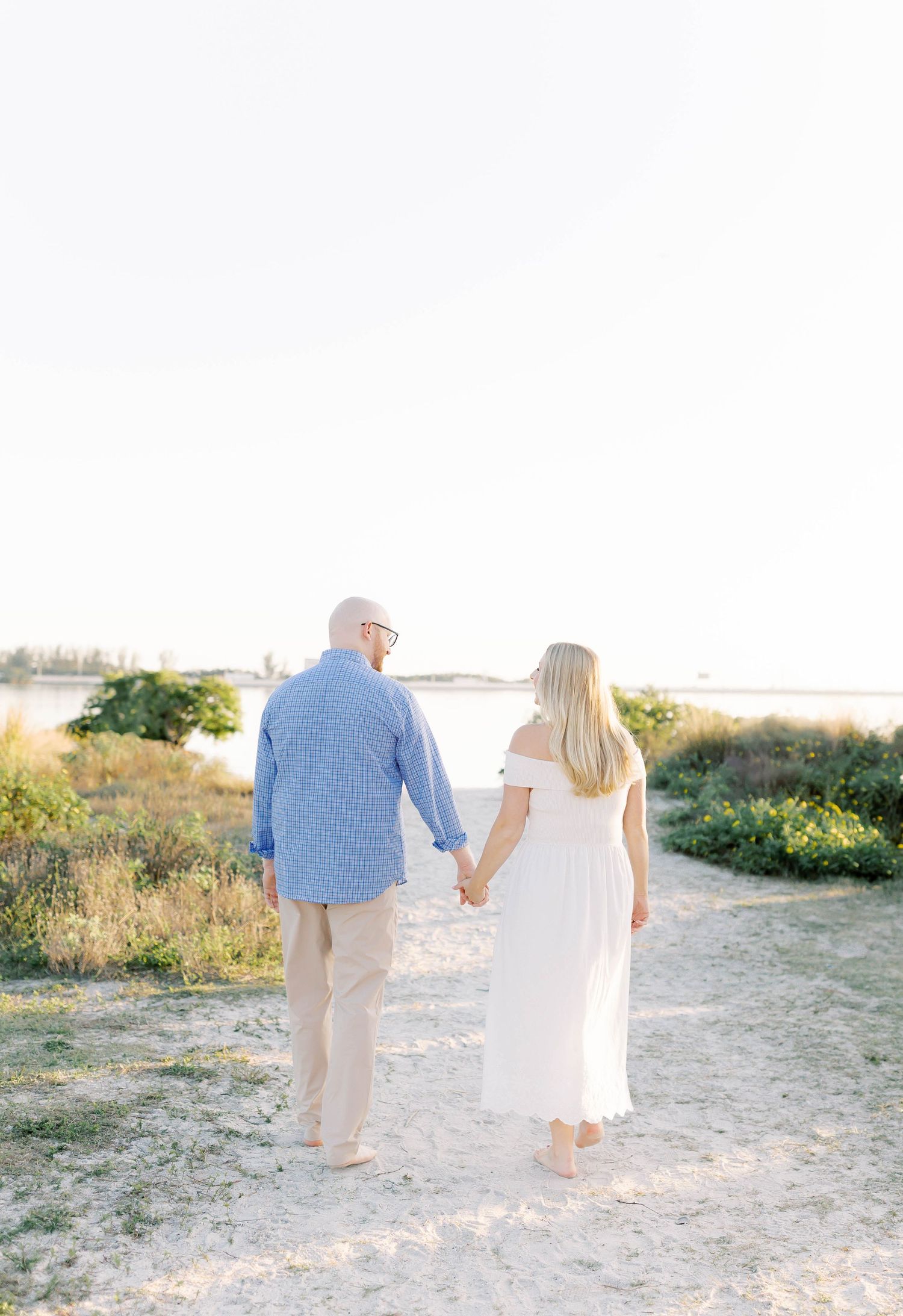 Couple walking hand in hand along sandy beach path at sunset.