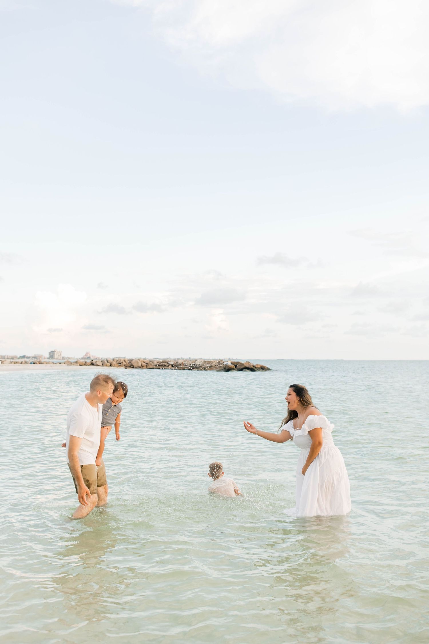 Family members splash and play in the shallow ocean waters wearing white clothing.
