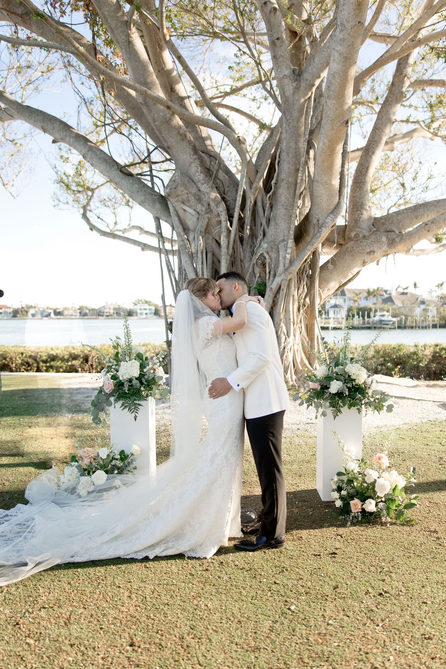 Wedding couple shares intimate moments under a large banyan tree with floral decorations.