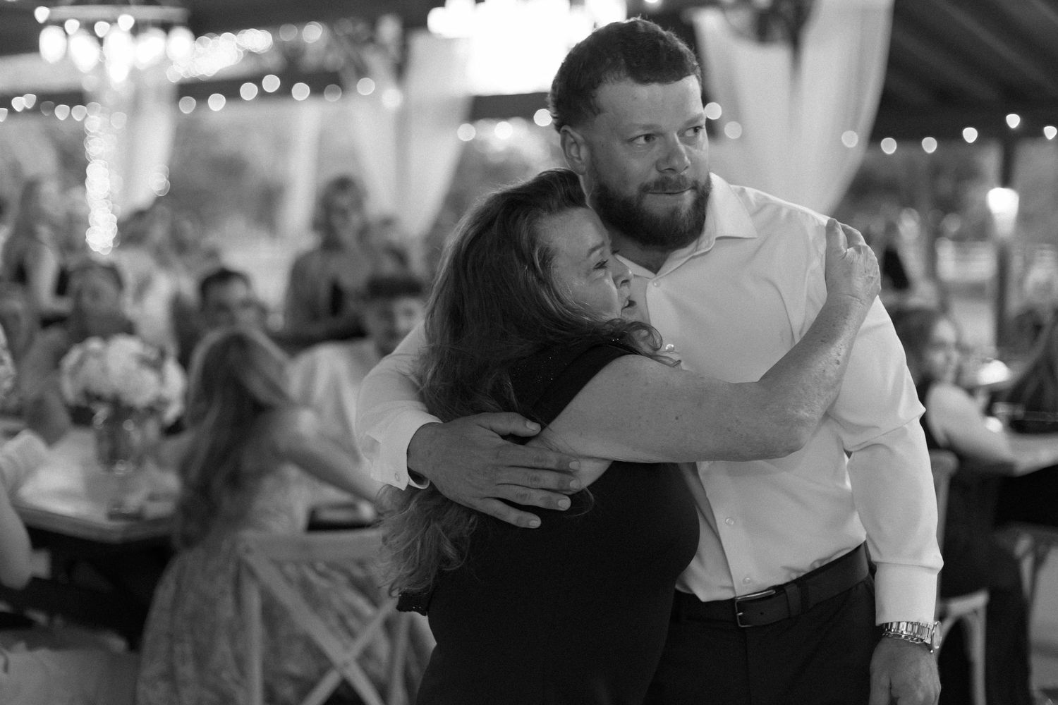 Black and white candid moment of couple dancing at reception with string lights overhead.