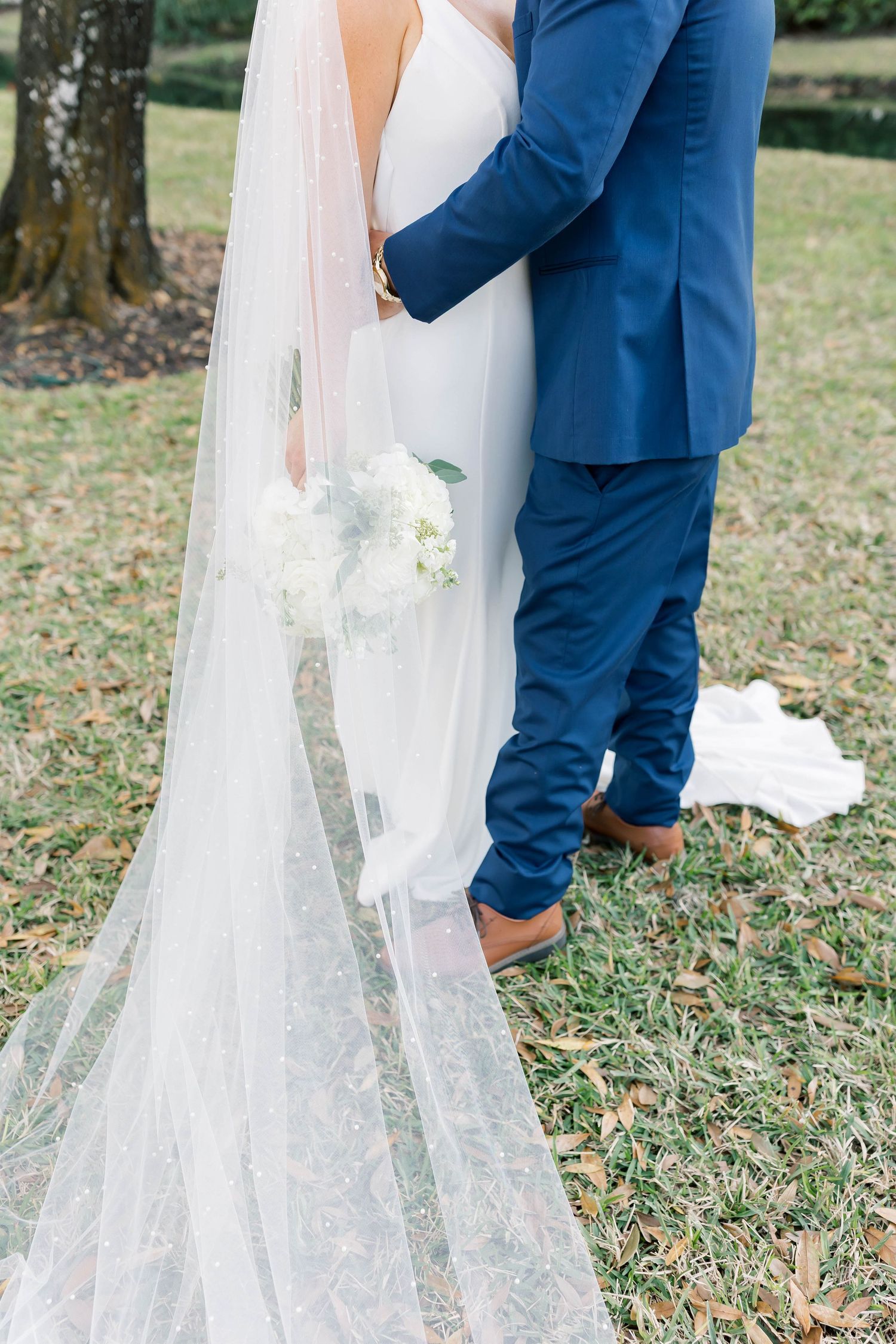 Close-up of wedding dress train and veil details on grass.