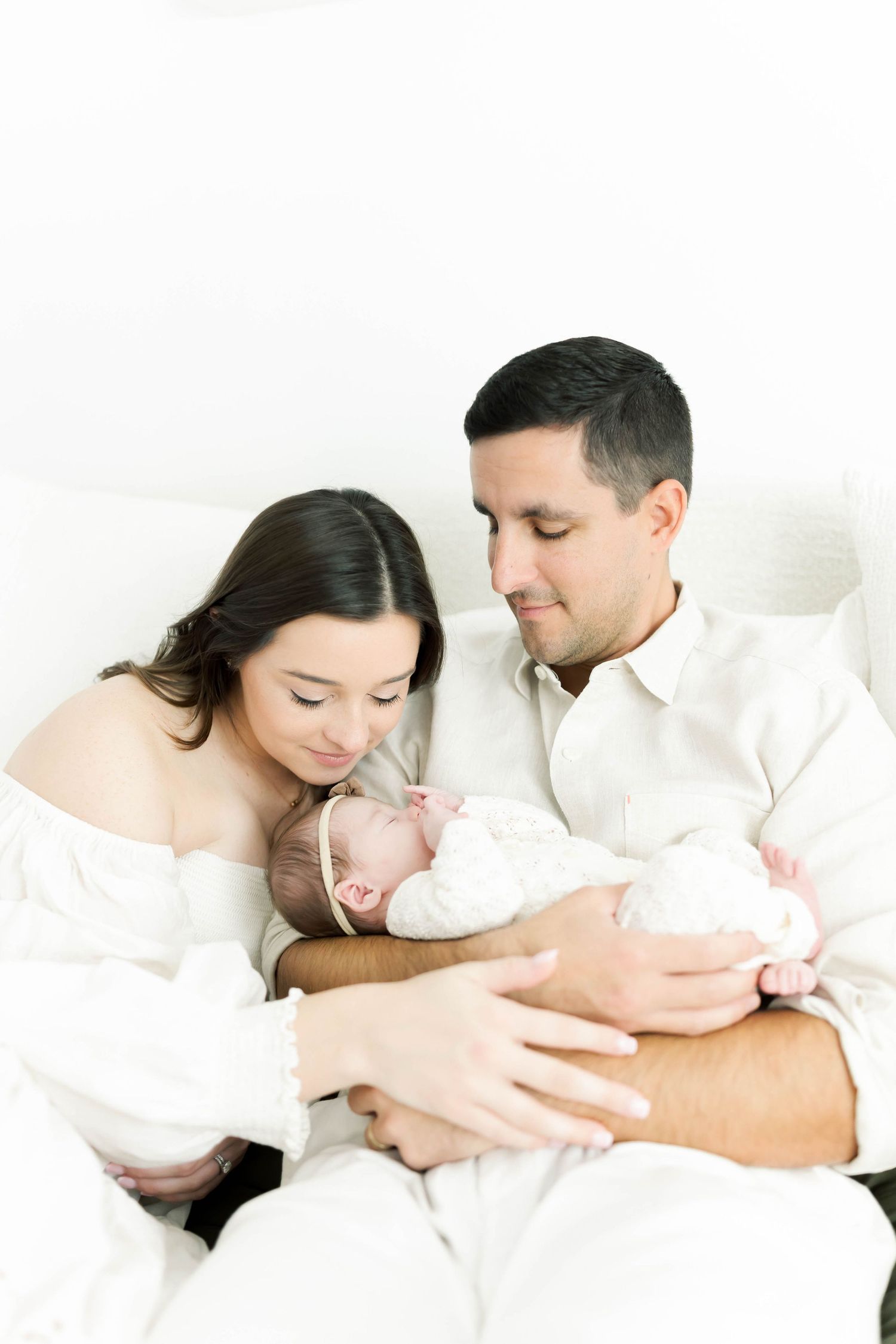 Artistic series of tender moments between parents and newborn in white setting.