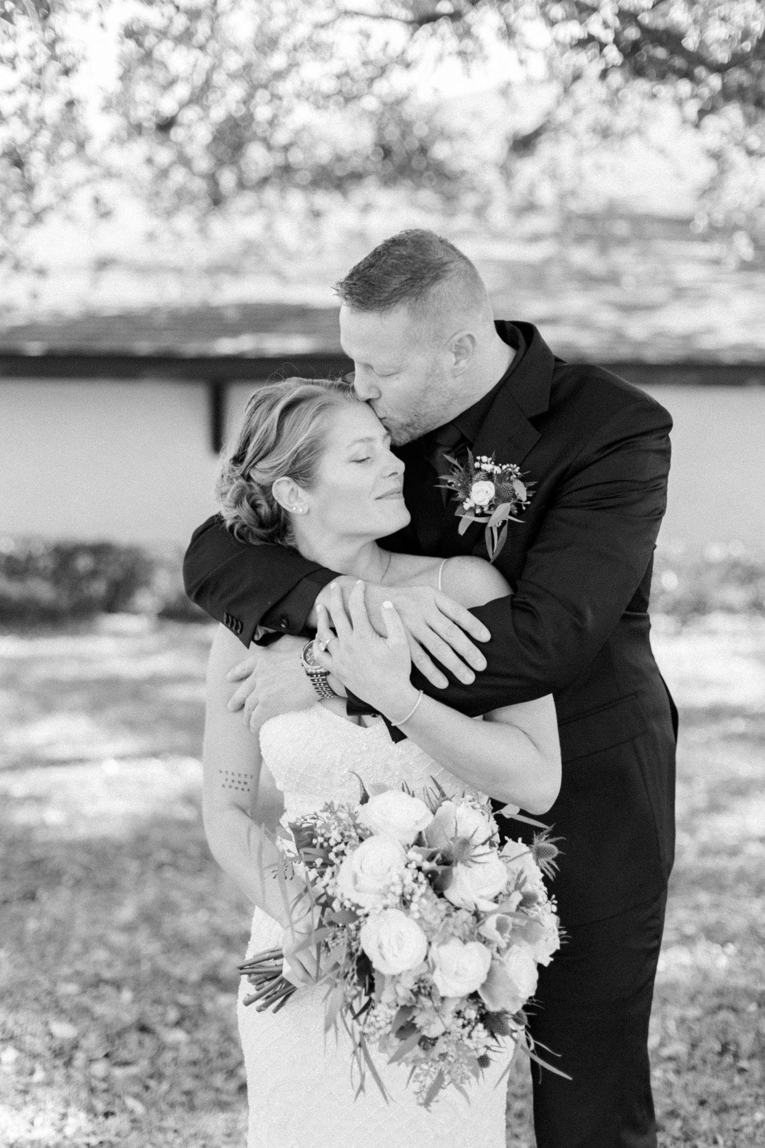 Intimate black and white portrait of newlyweds sharing tender moment outdoors.