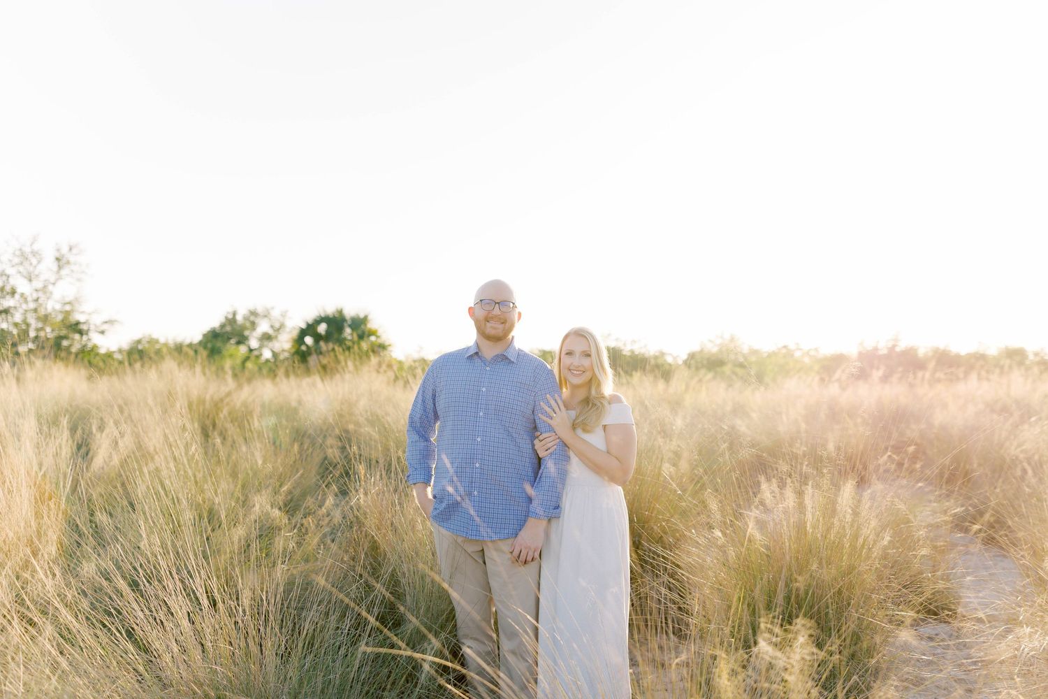 Romantic couple standing in sunlit field of tall grass during golden hour.