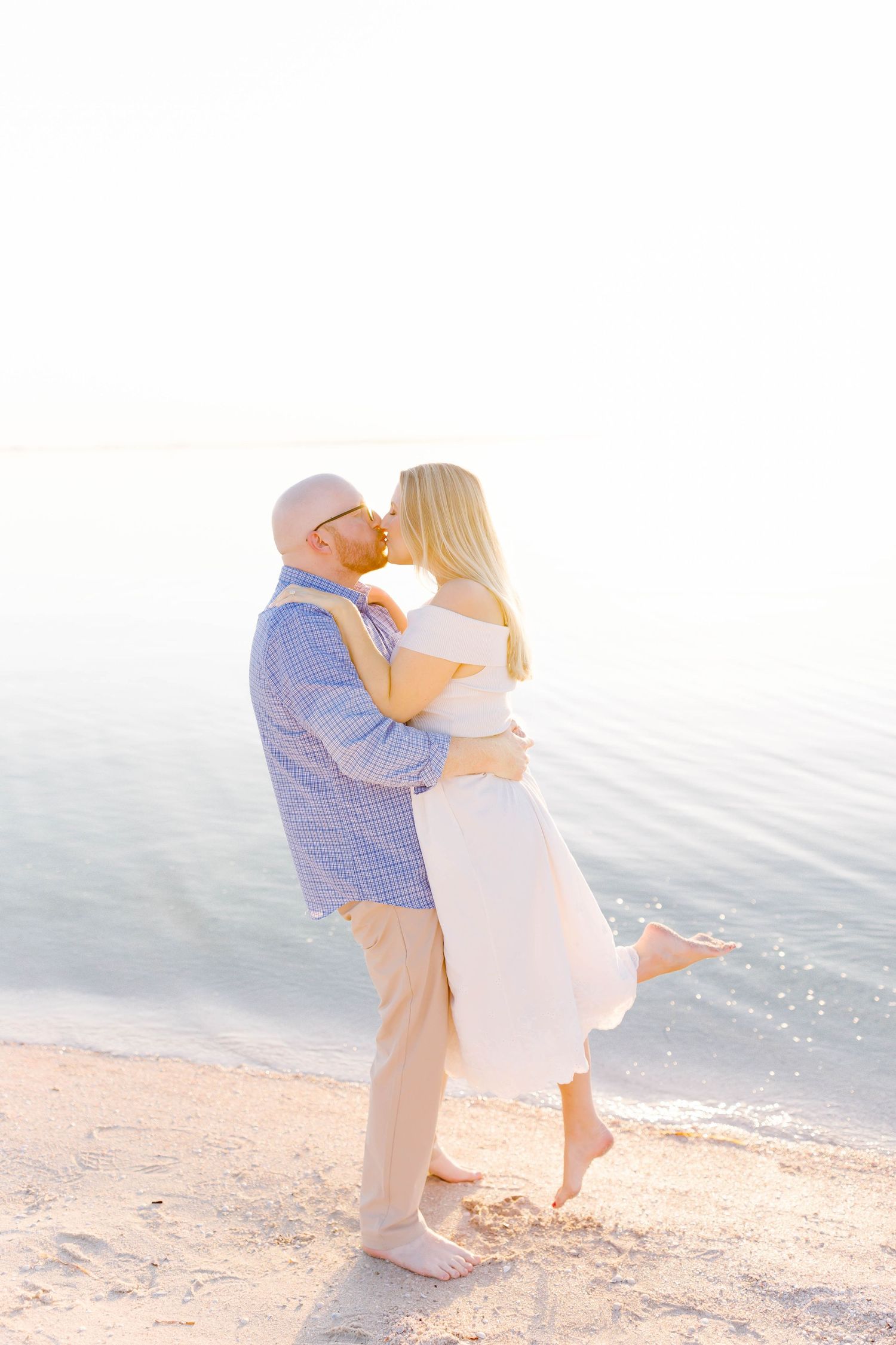 Couple embracing on a beach with soft sunset lighting and ocean waves in the background.