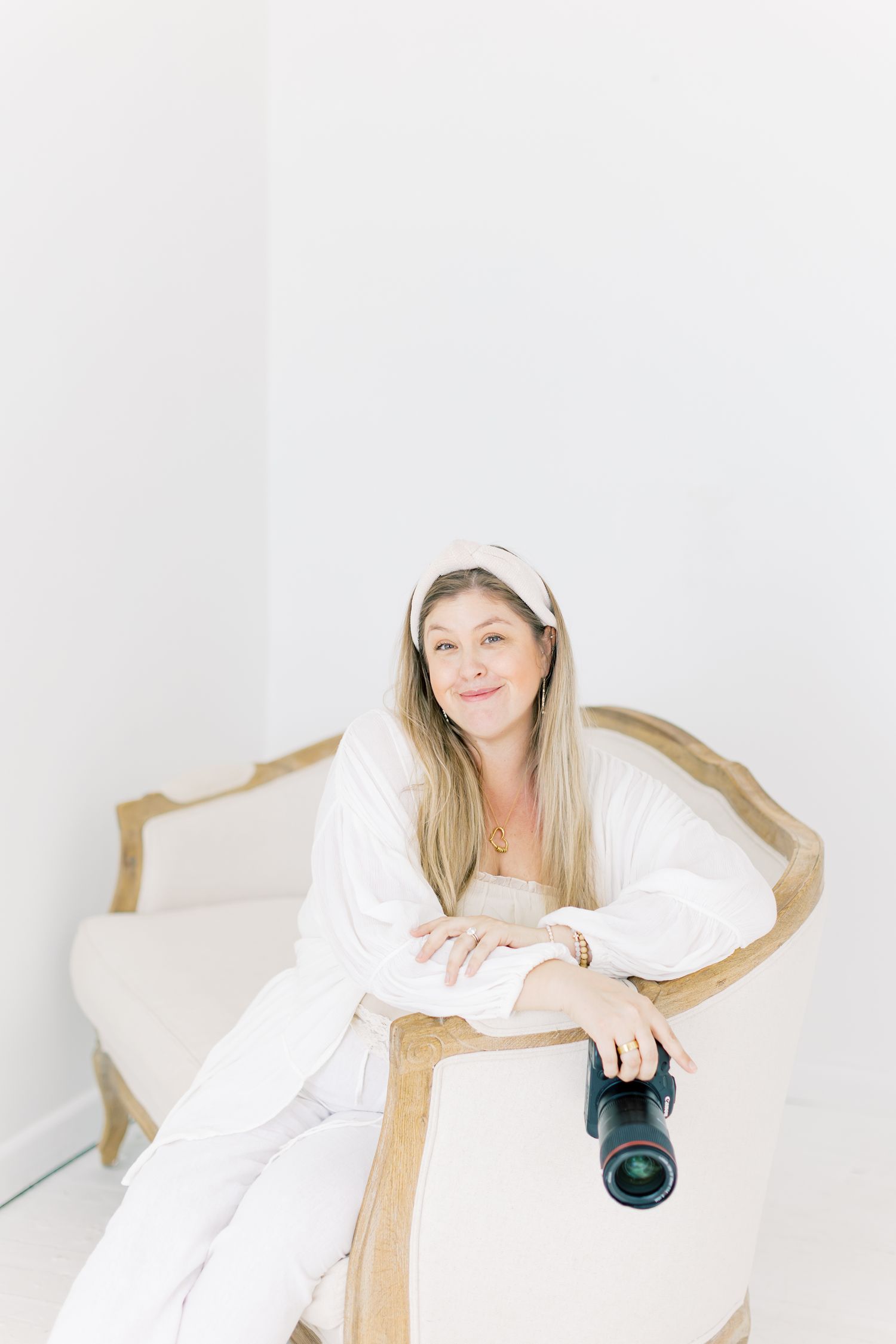 Professional photographer in white robe relaxes on vintage chair while holding camera.