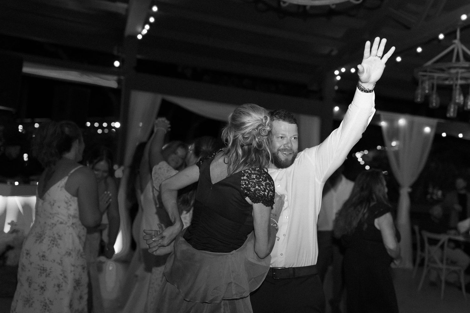 Wedding guests dancing and celebrating on a dimly lit dance floor at a reception.
