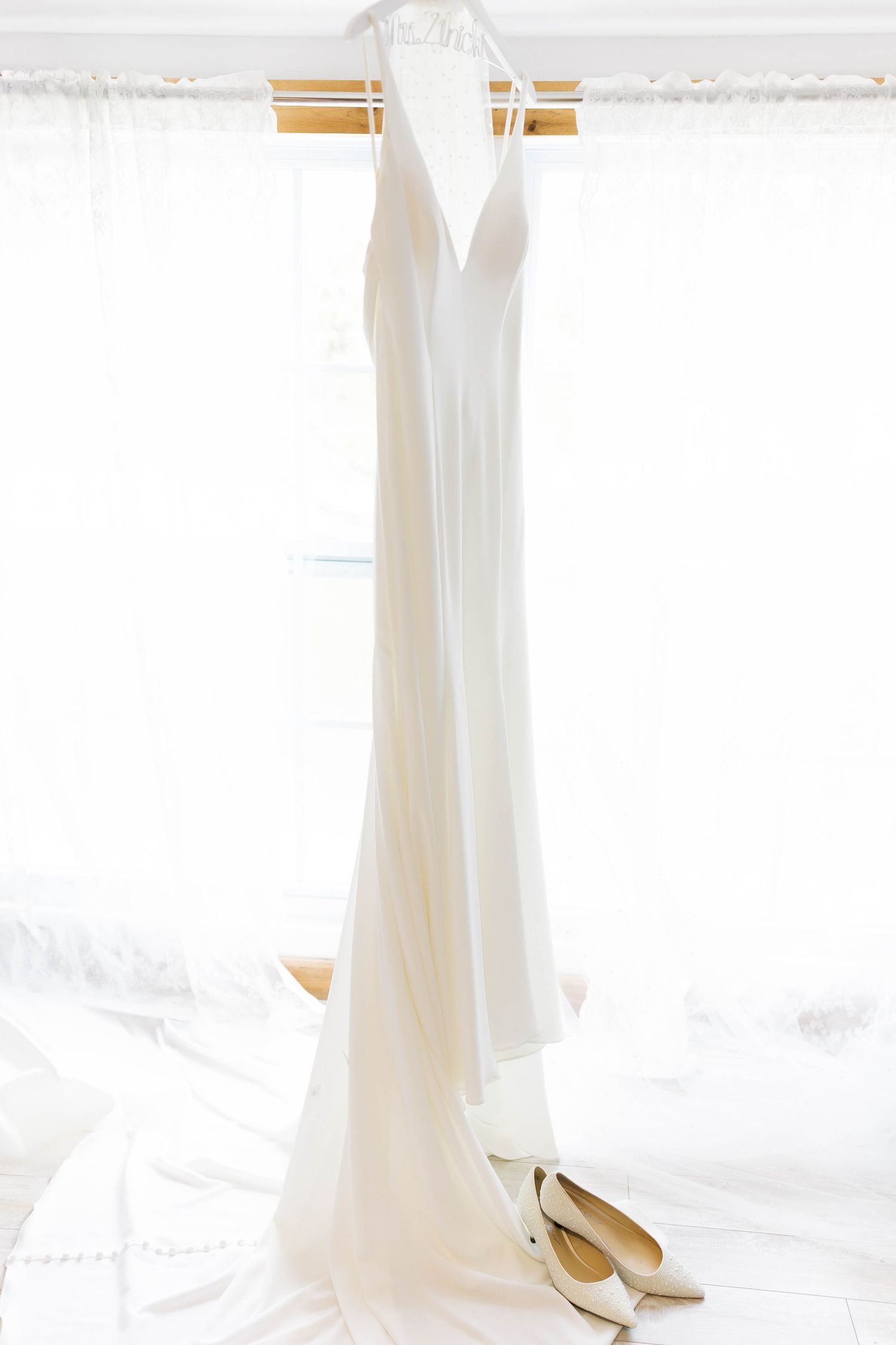 White wedding dress hanging against a bright window with natural light.
