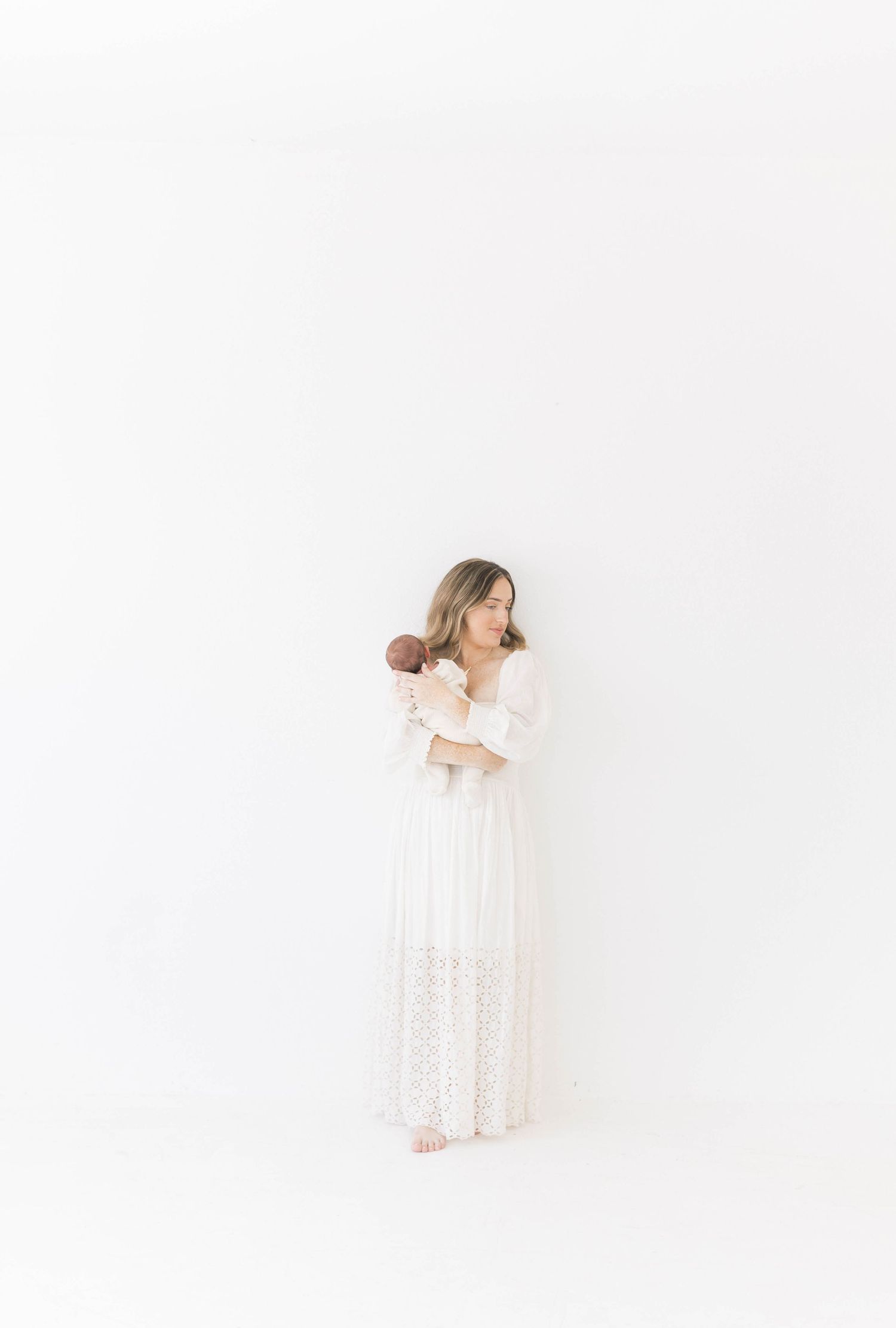Family portrait in white clothing against minimalist studio backdrop.