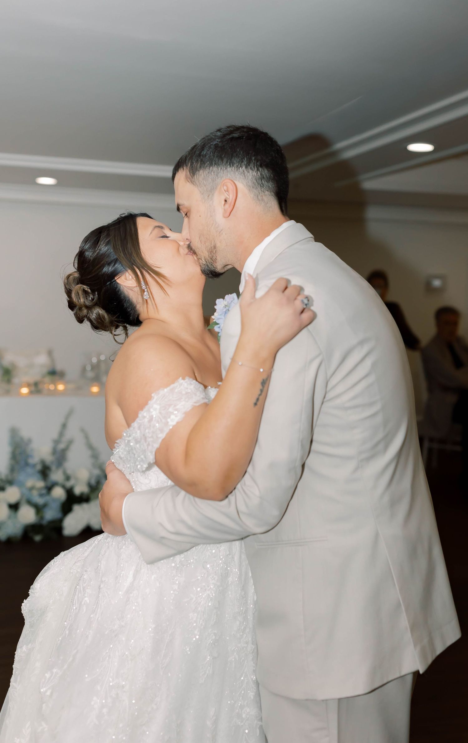 Bride and groom share romantic first dance kiss in elegant white and blue reception venue.