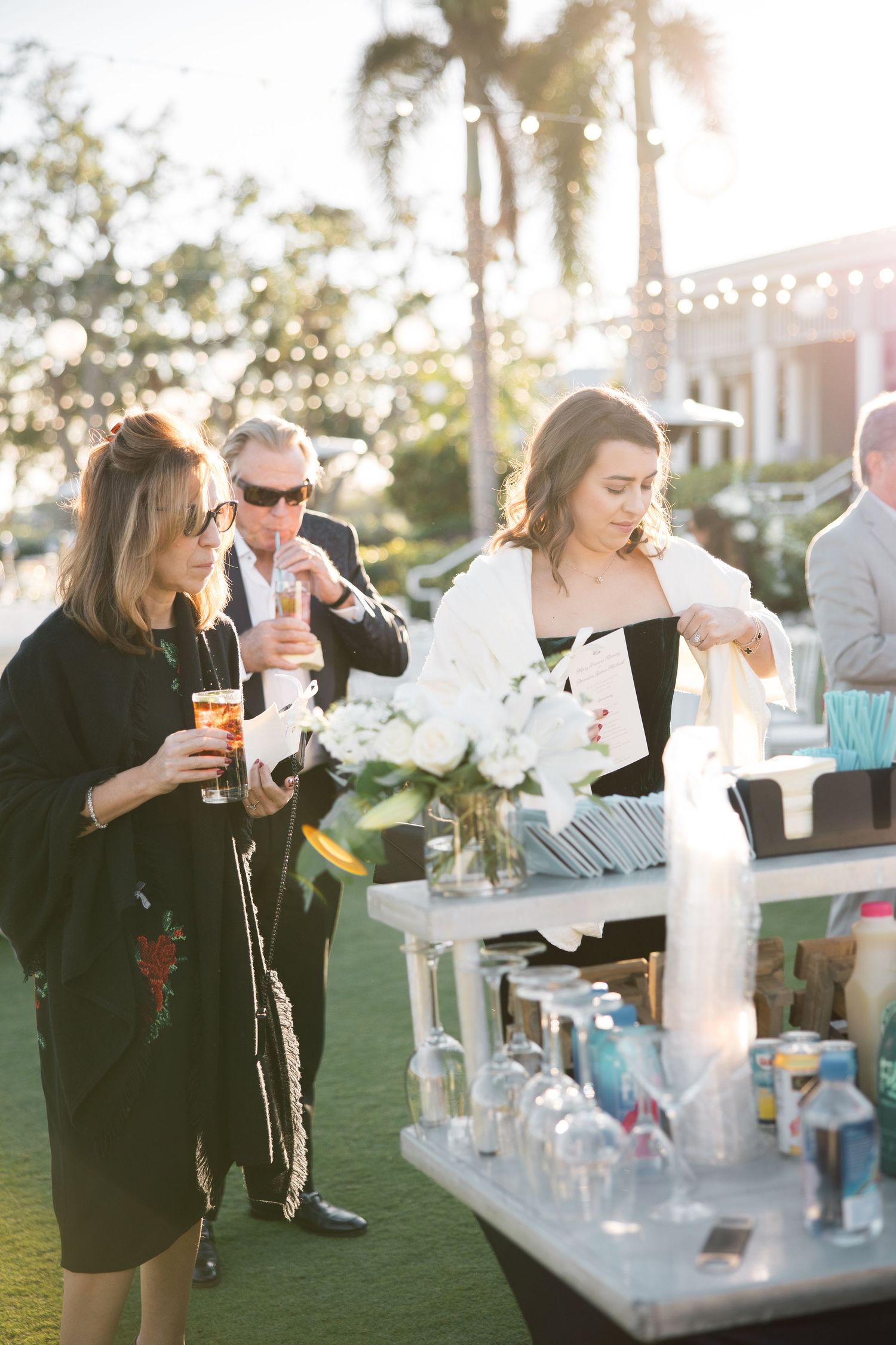 Guests mingling at an outdoor cocktail bar with string lights overhead.