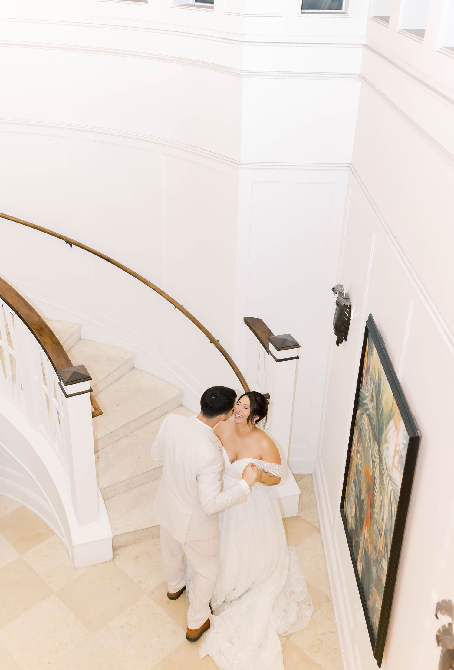 Aerial view of bride and groom sharing a romantic embrace on an elegant curved staircase indoors.