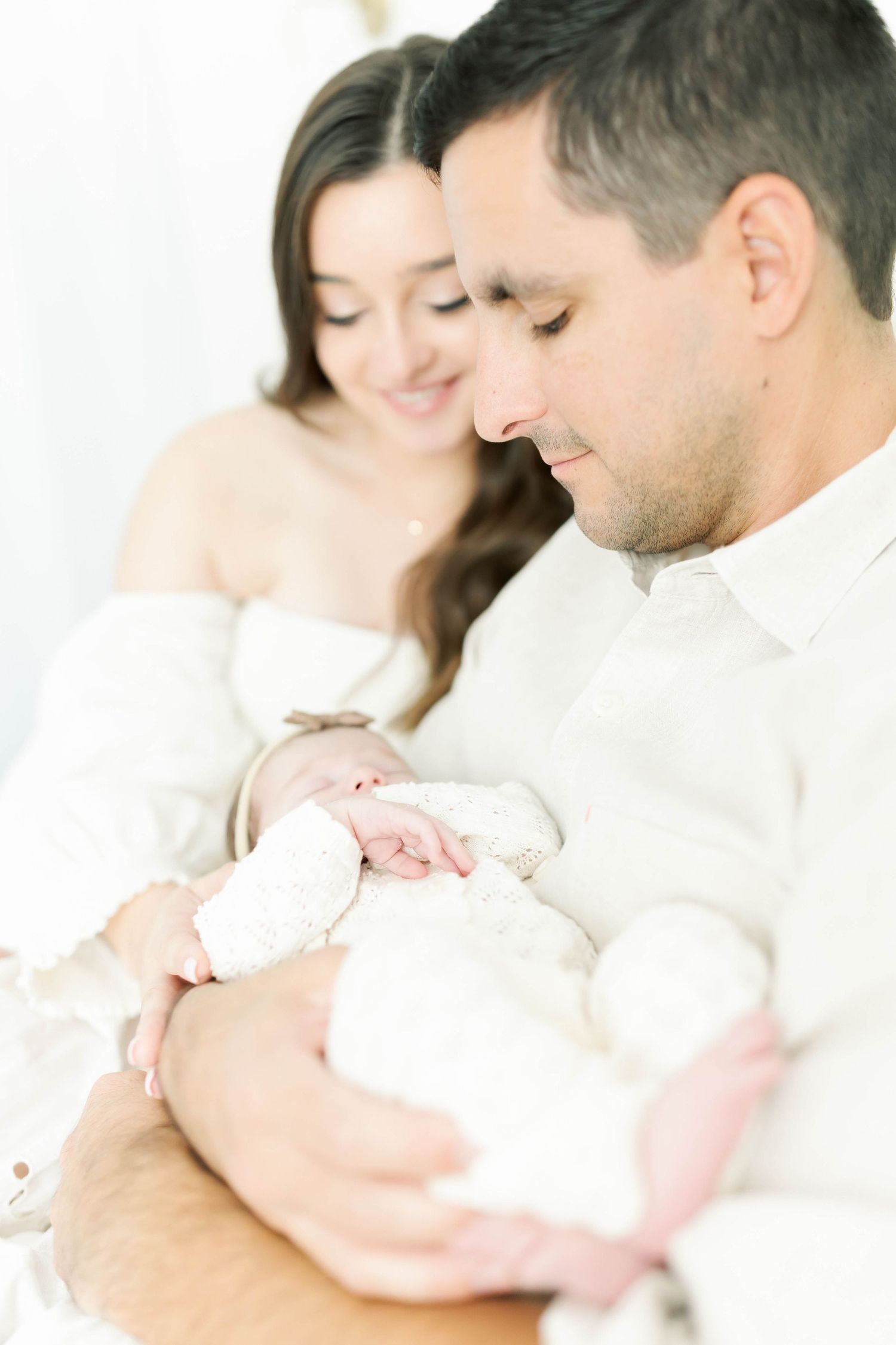 Family sharing tender moments with newborn baby in white themed photoshoot.