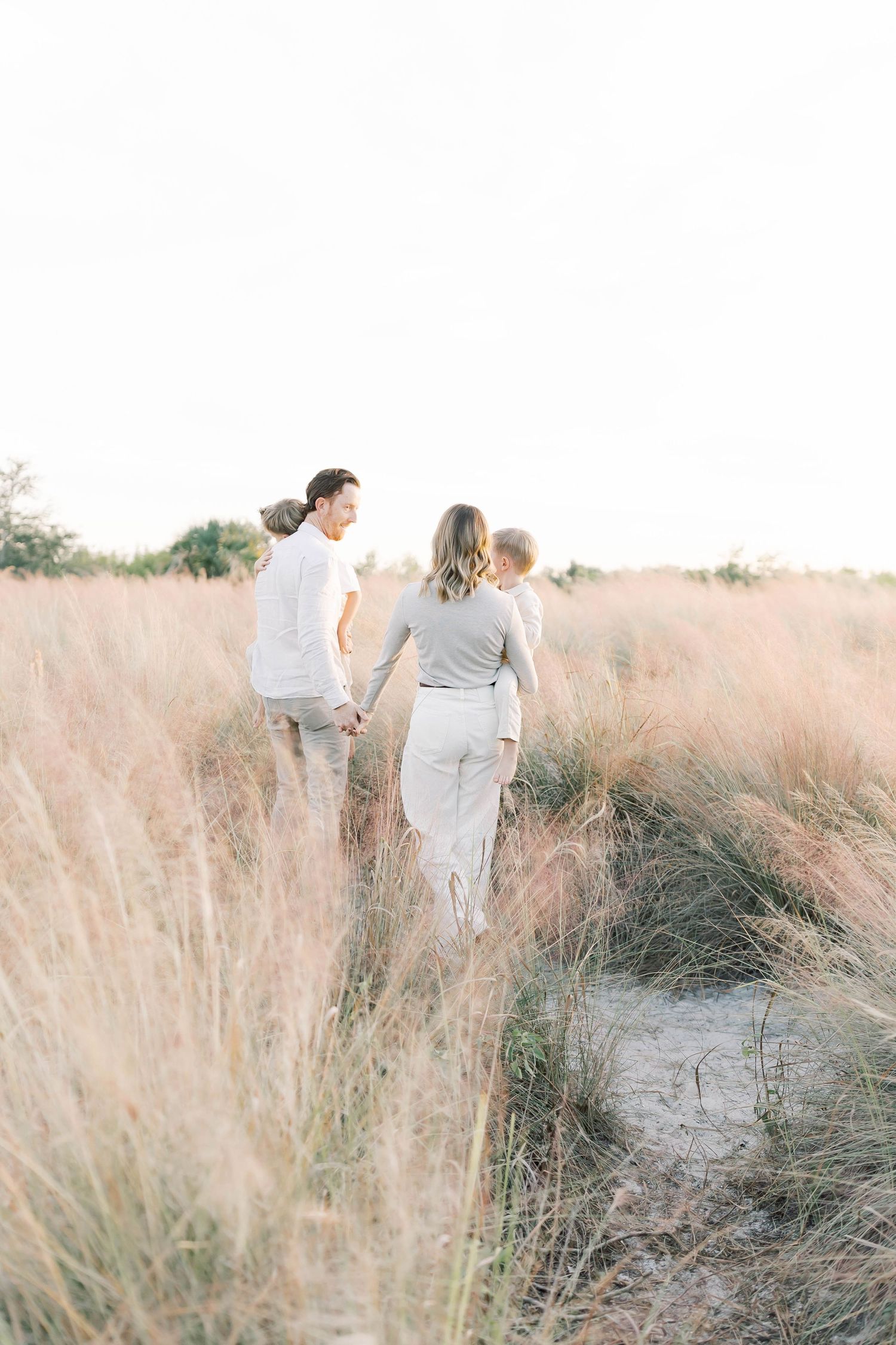 Family walks through tall grass during golden hour wearing coordinated neutral outfits.