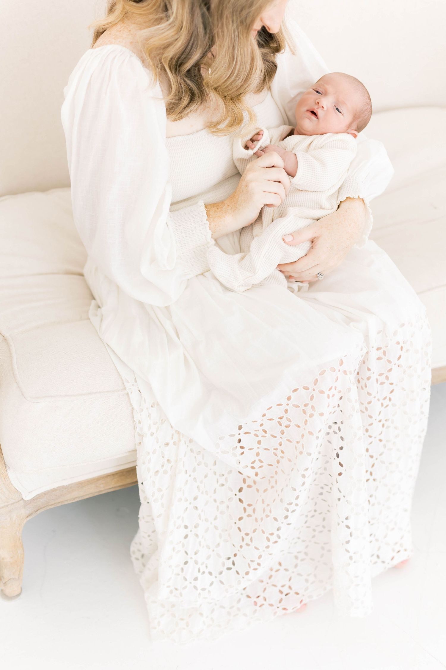Tender newborn photography session with white lace dress and soft lighting on white backdrop.