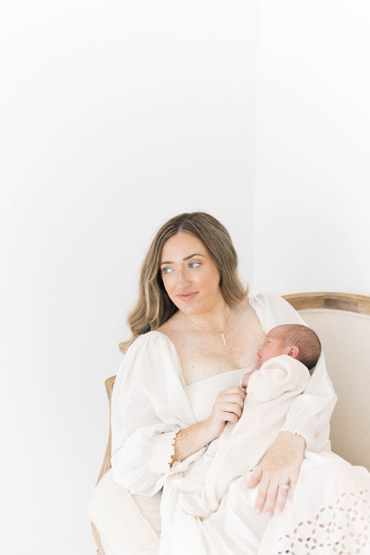 Intimate newborn photography session with mother and baby in soft white setting.