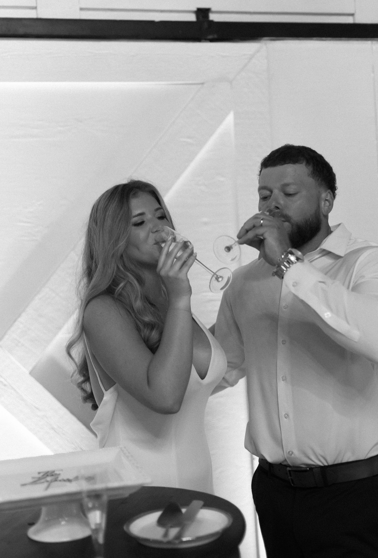 Black and white photo of couple sharing champagne during wedding reception.