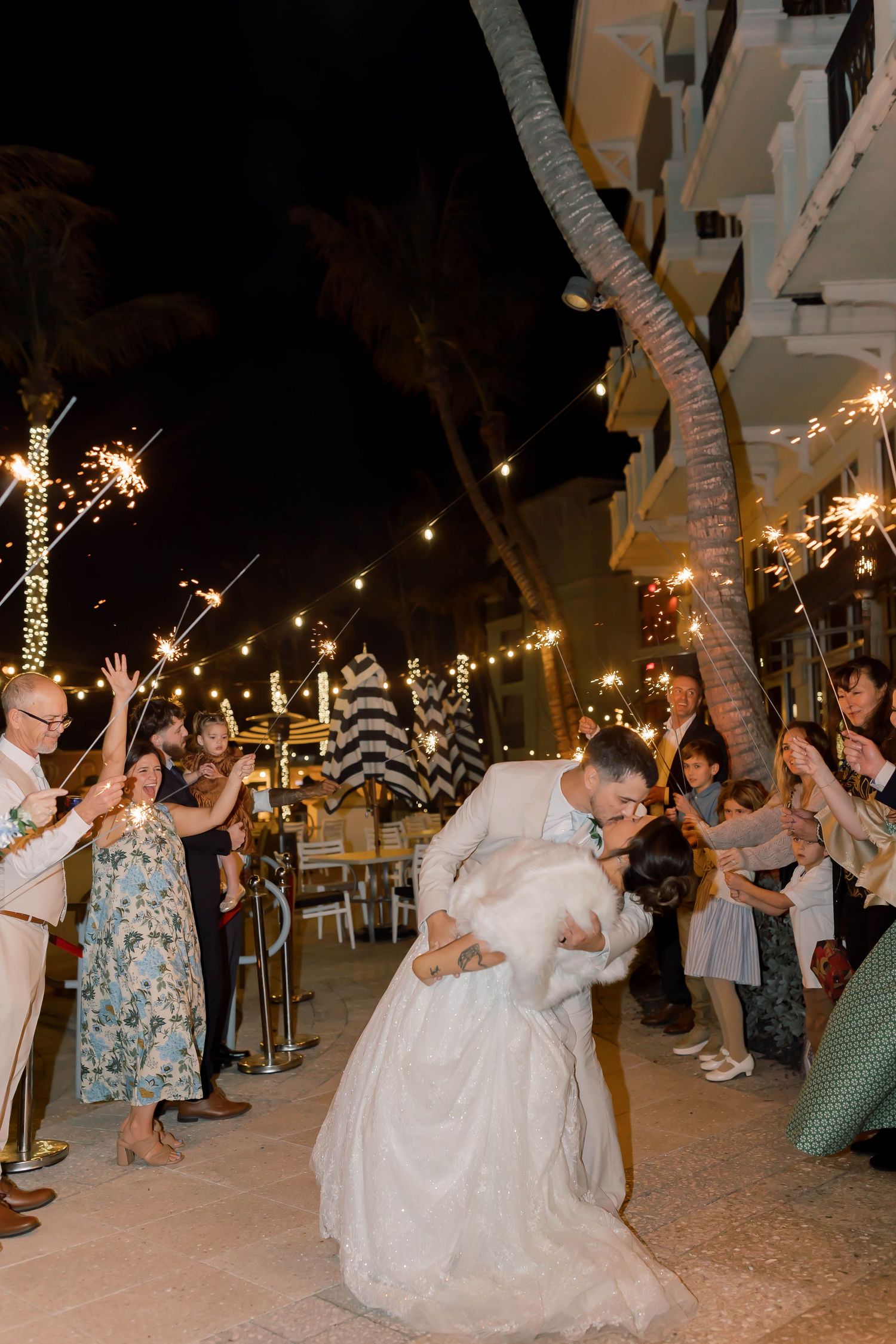 Groom dips bride during sparkler exit as wedding guests celebrate at a nighttime outdoor reception.