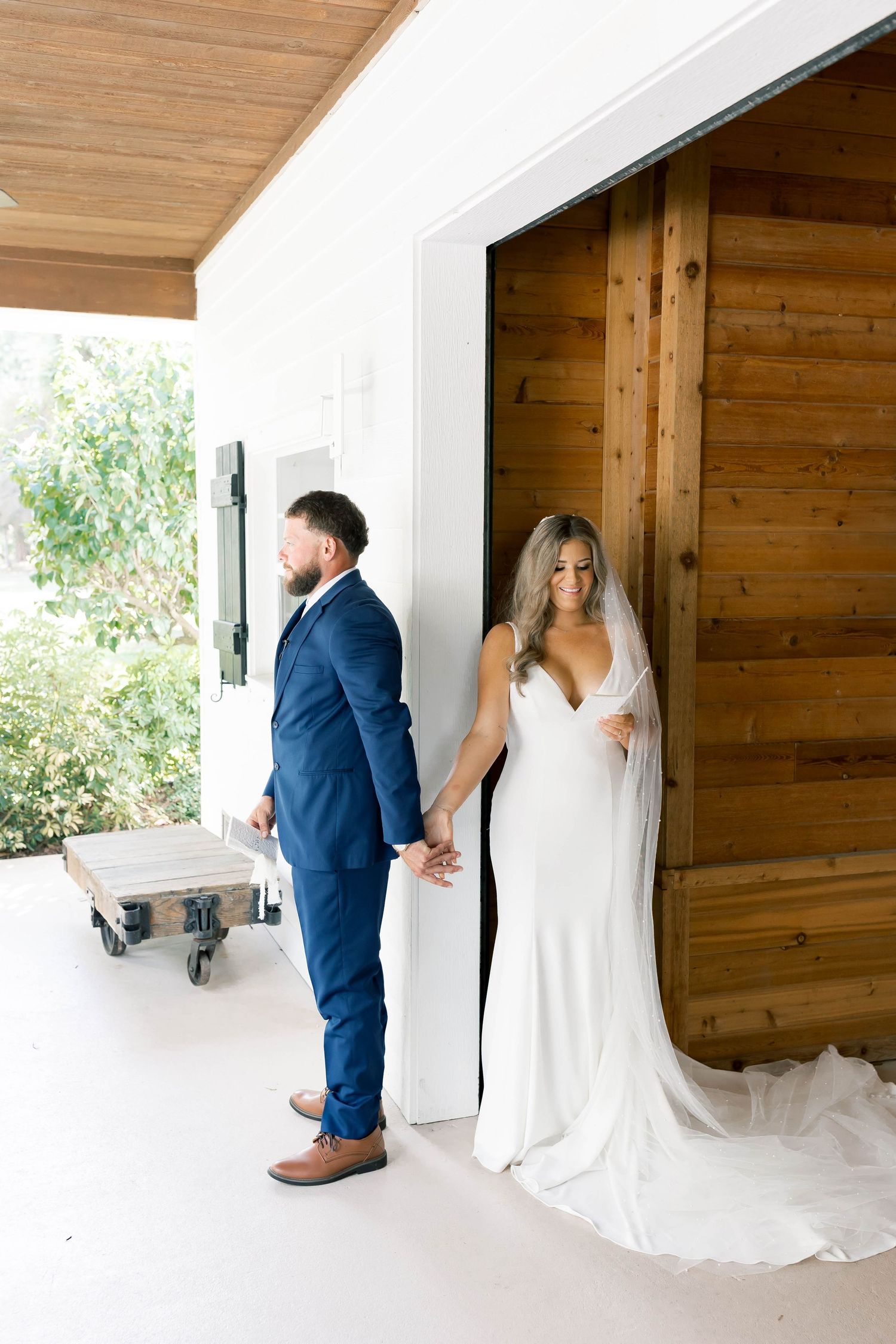 First look wedding moment through wooden window between couple in blue suit and white dress.