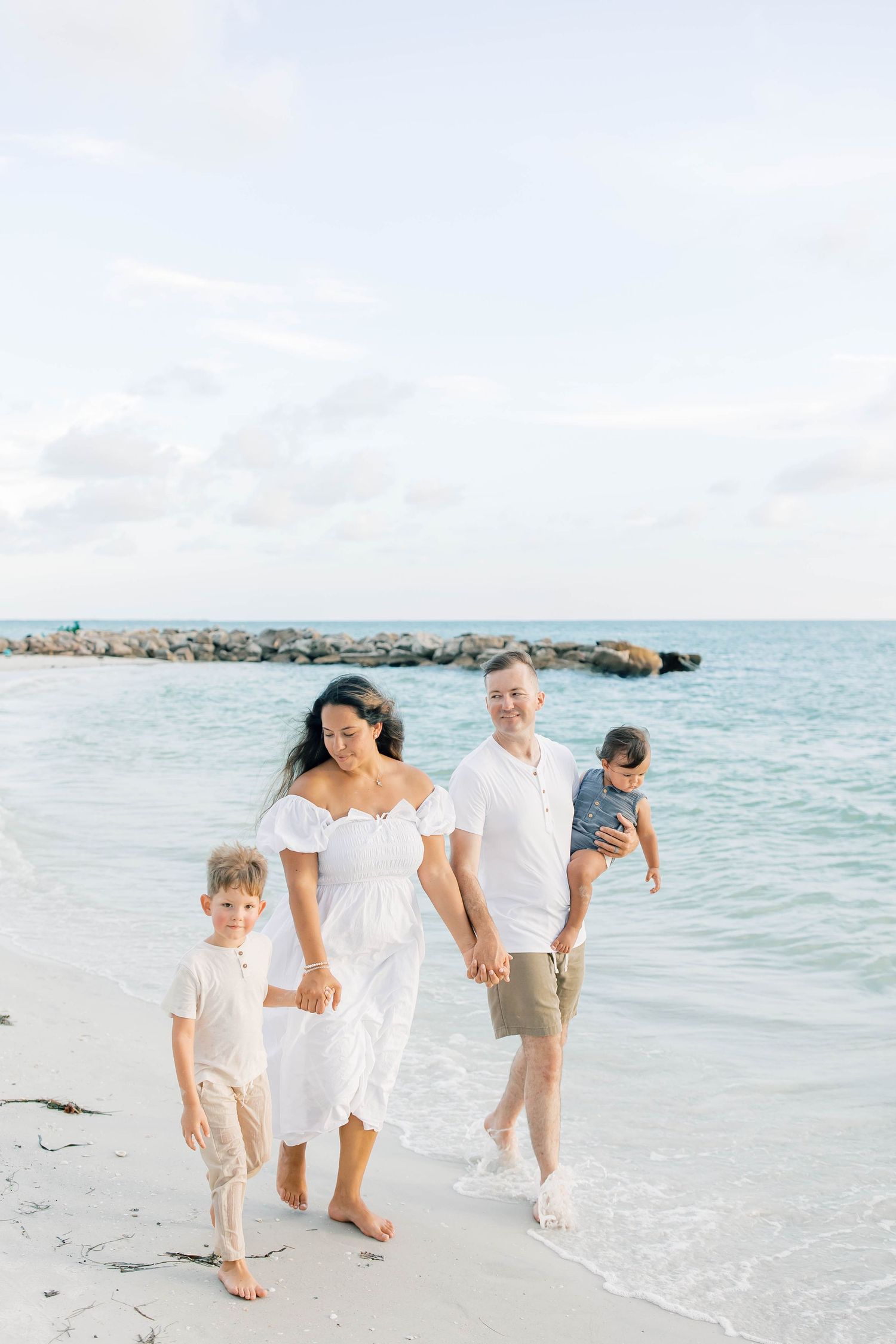 A family walks together along a white sandy beach with turquoise waters in the background.