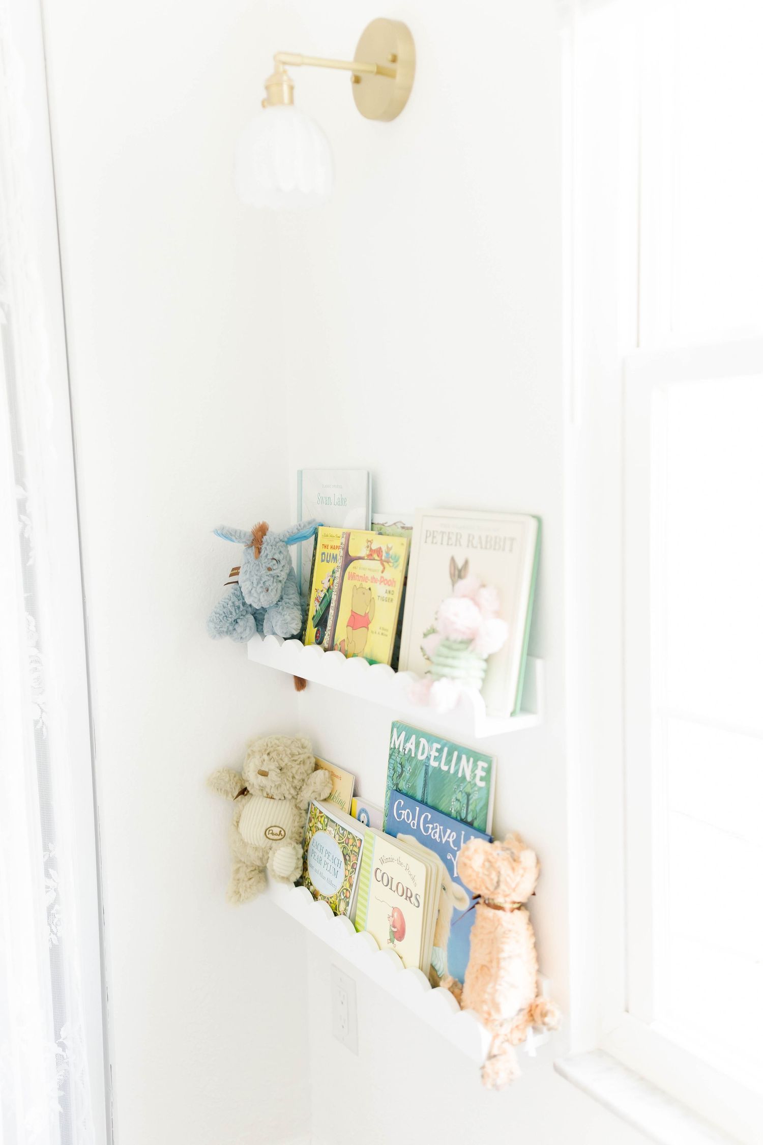 Nursery bookshelf displaying children's books and stuffed animals against white wall.