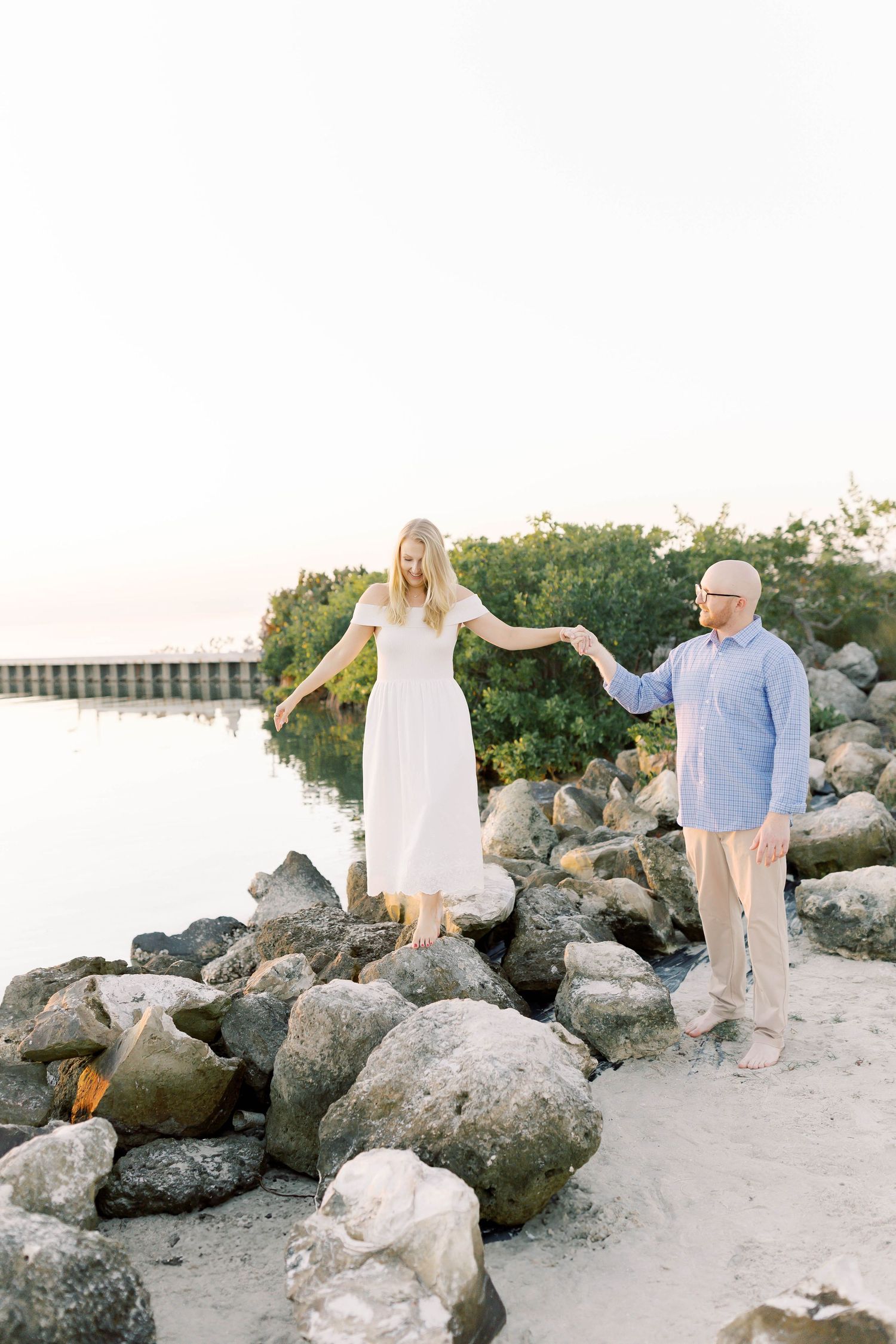 Playful couple poses on rocky beach during sunset photoshoot.