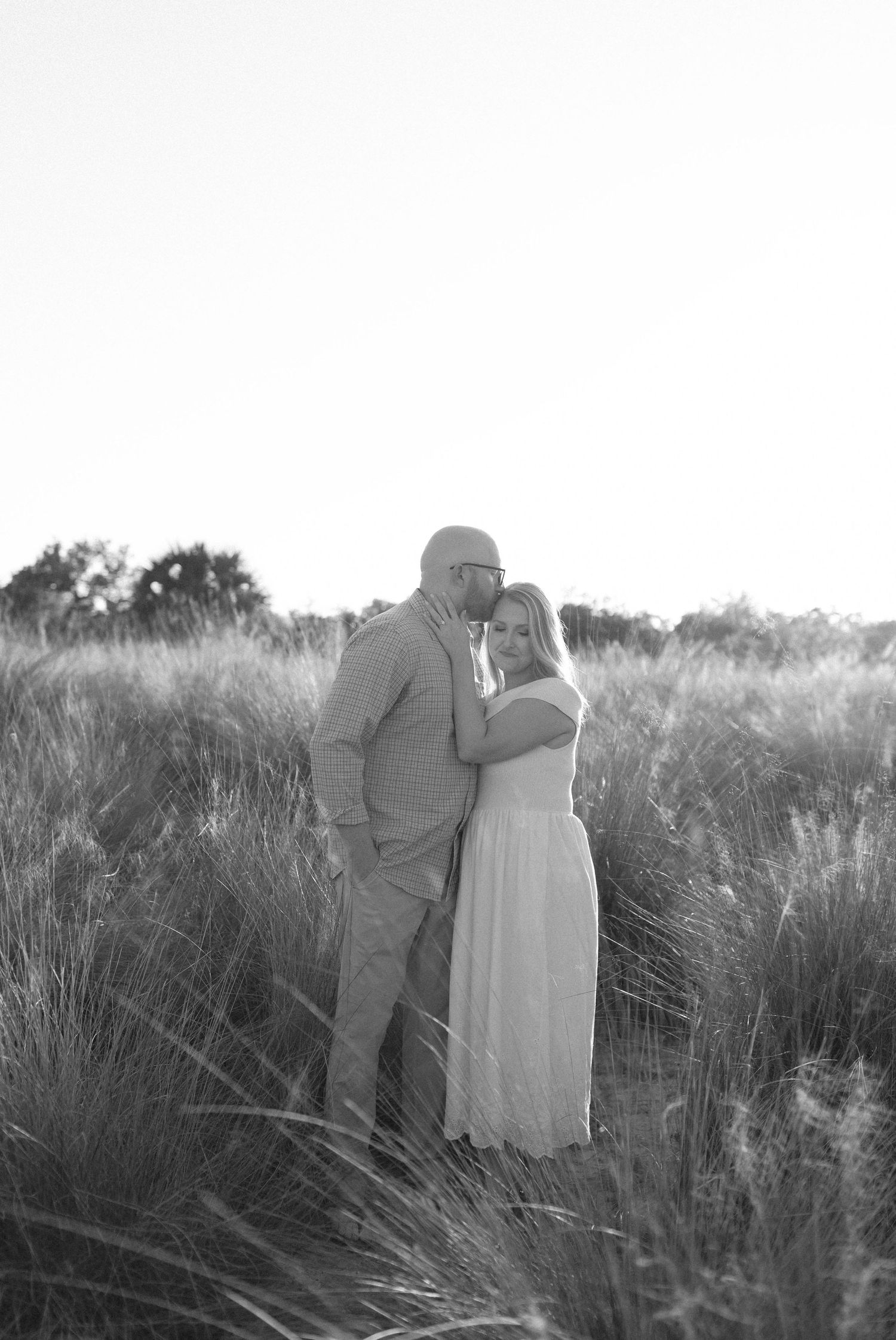 Black and white portrait of a couple embracing in a field of tall grass.