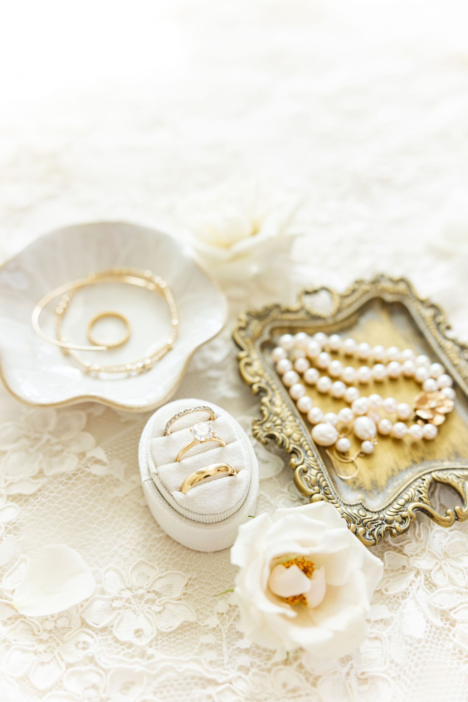 Wedding accessories including pearl necklaces and ring dishes arranged on white lace.