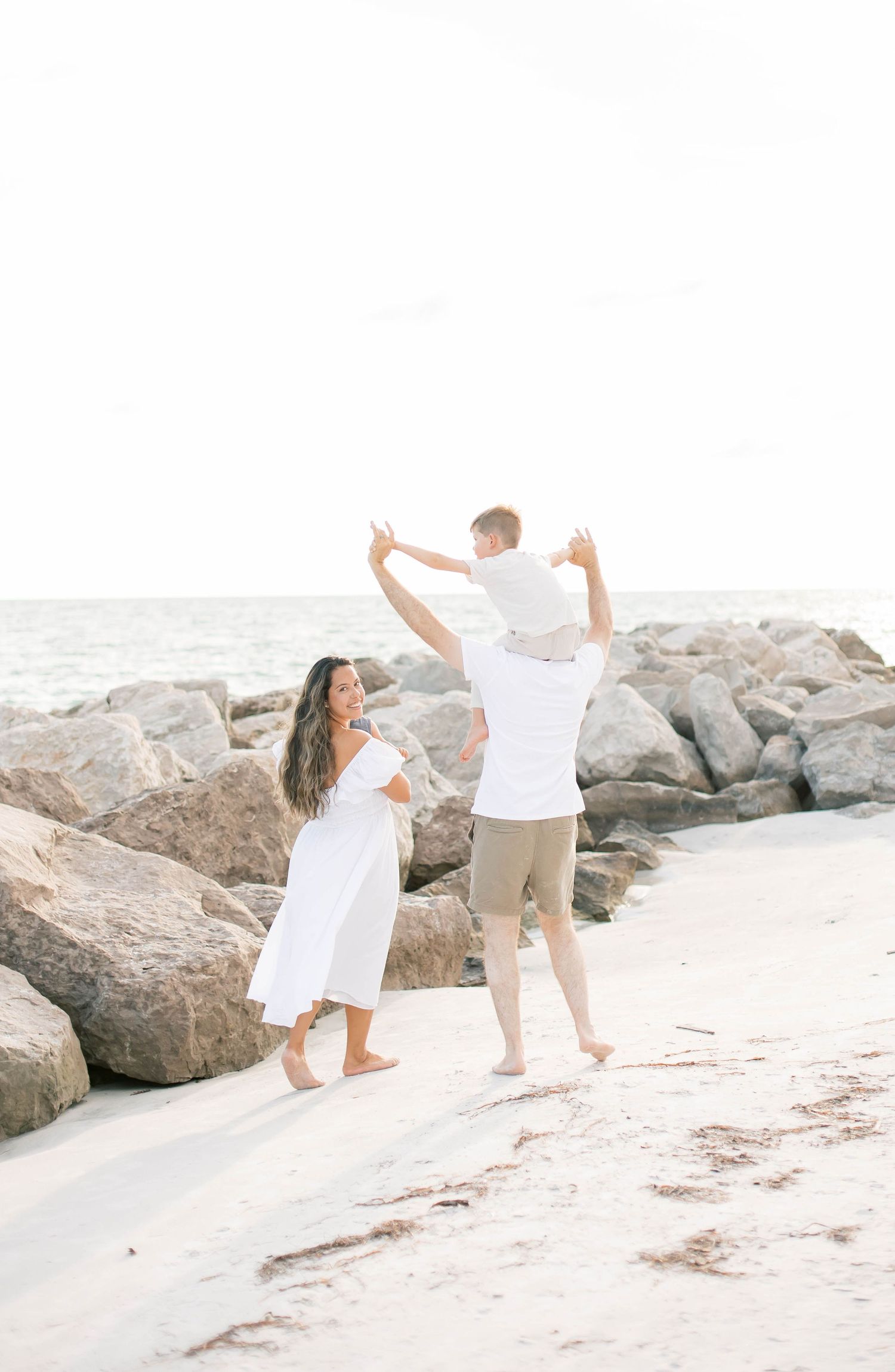 Family members dancing and celebrating together on a sunny beach with rocky backdrop.