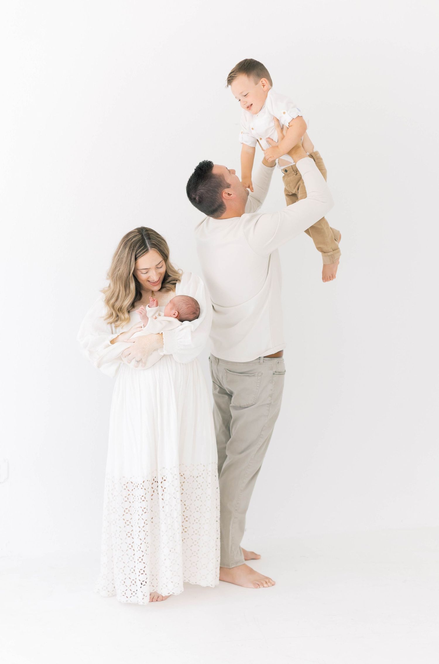 Family dressed in white and neutral tones sharing playful moments in studio setting.