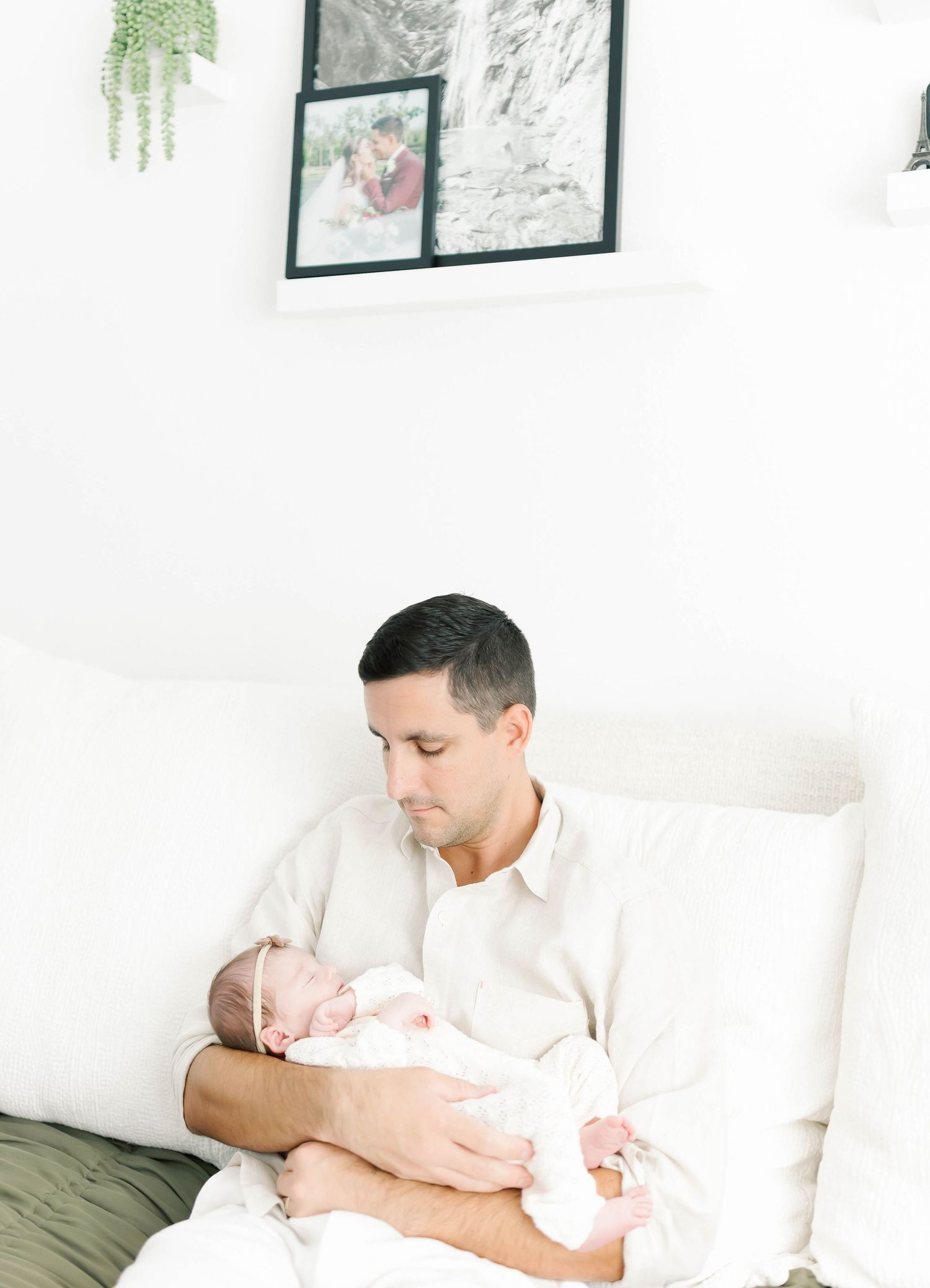 Parent in white shirt holding sleeping newborn baby on white couch.