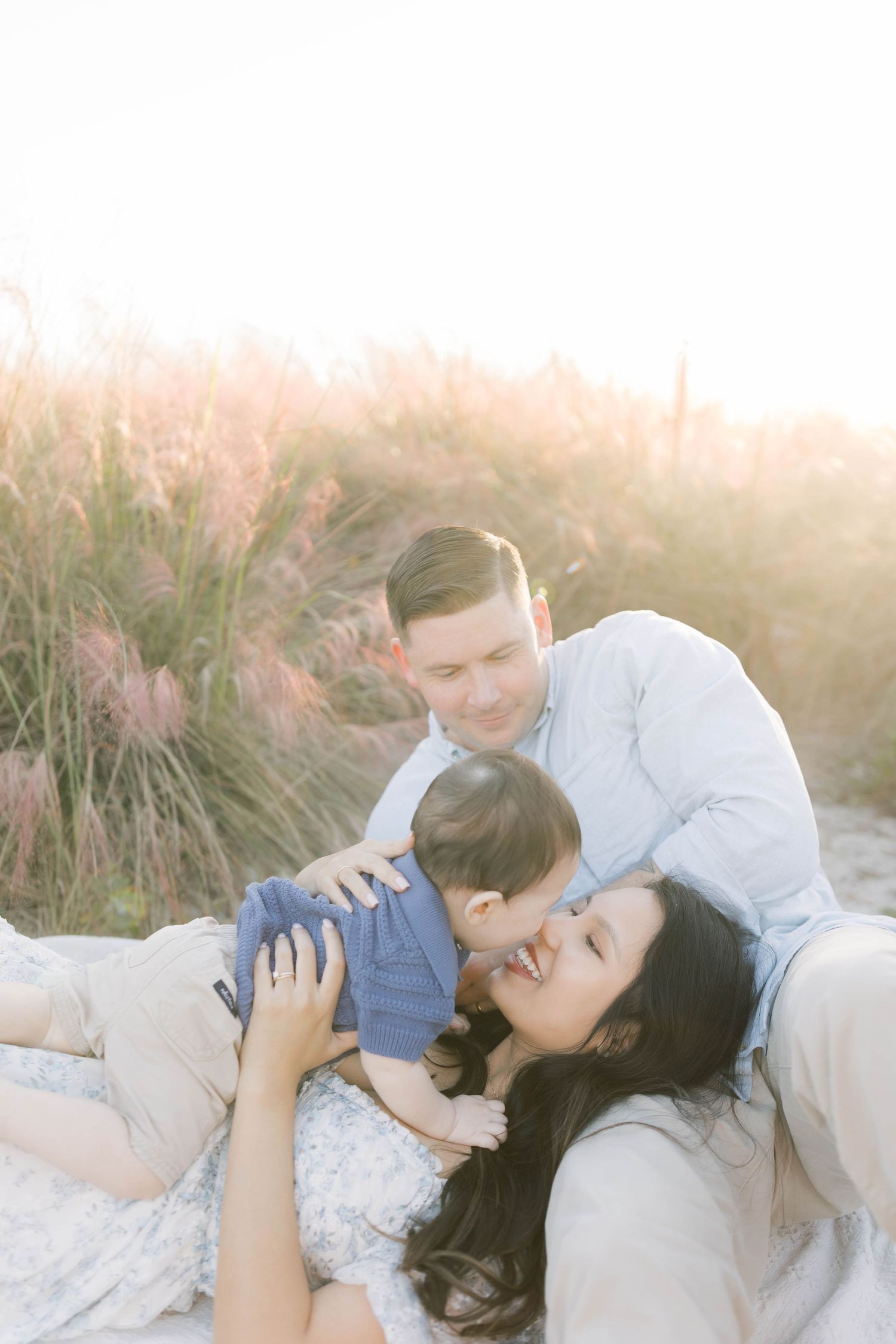 Couple lying together romantically in beach grass during golden hour.