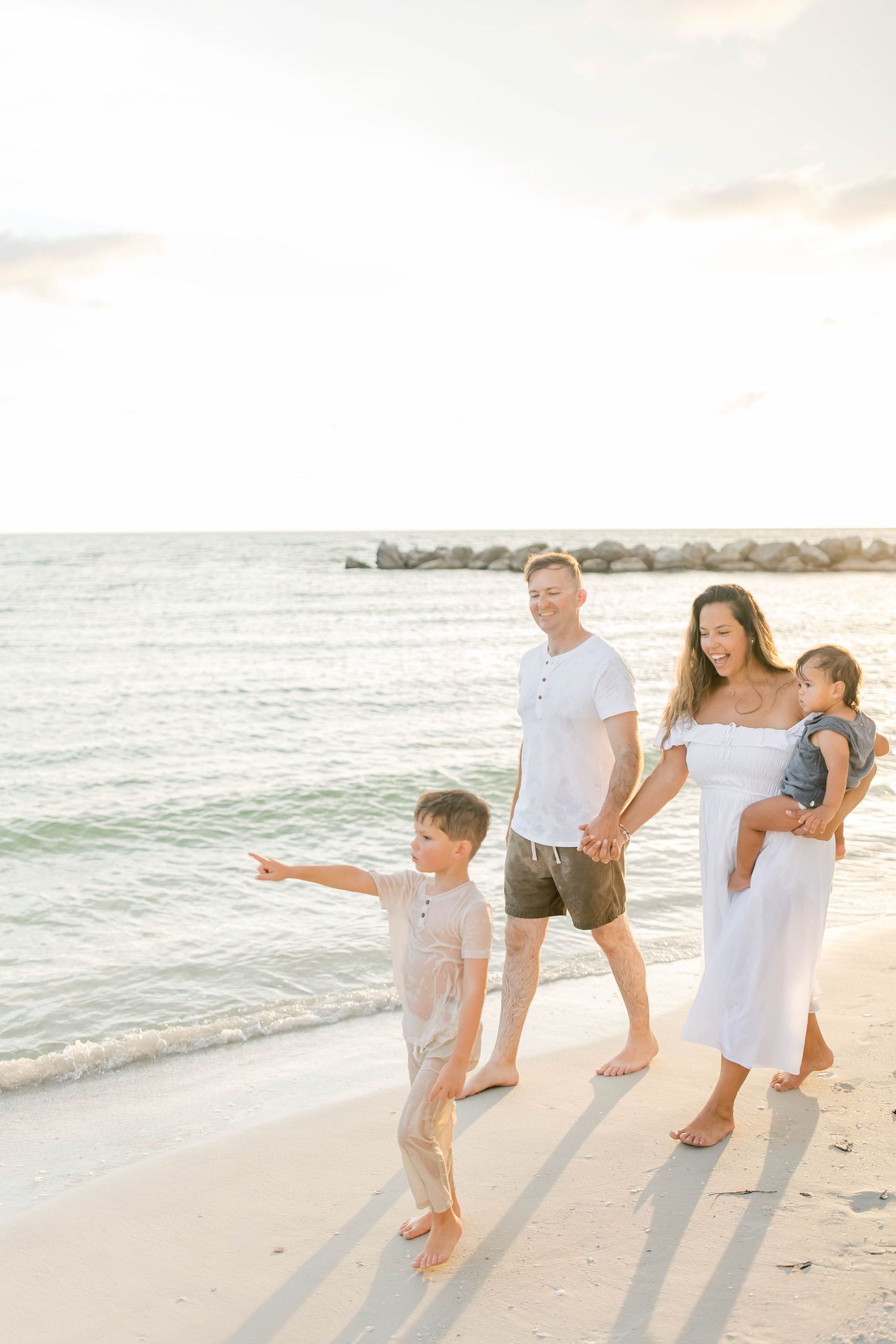 Family enjoying a playful moment together on a sunny beach with gentle waves in the background.