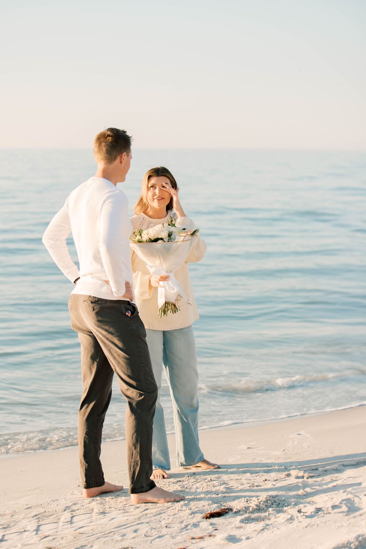 A couple enjoys a playful moment together on a white sandy beach at sunset.