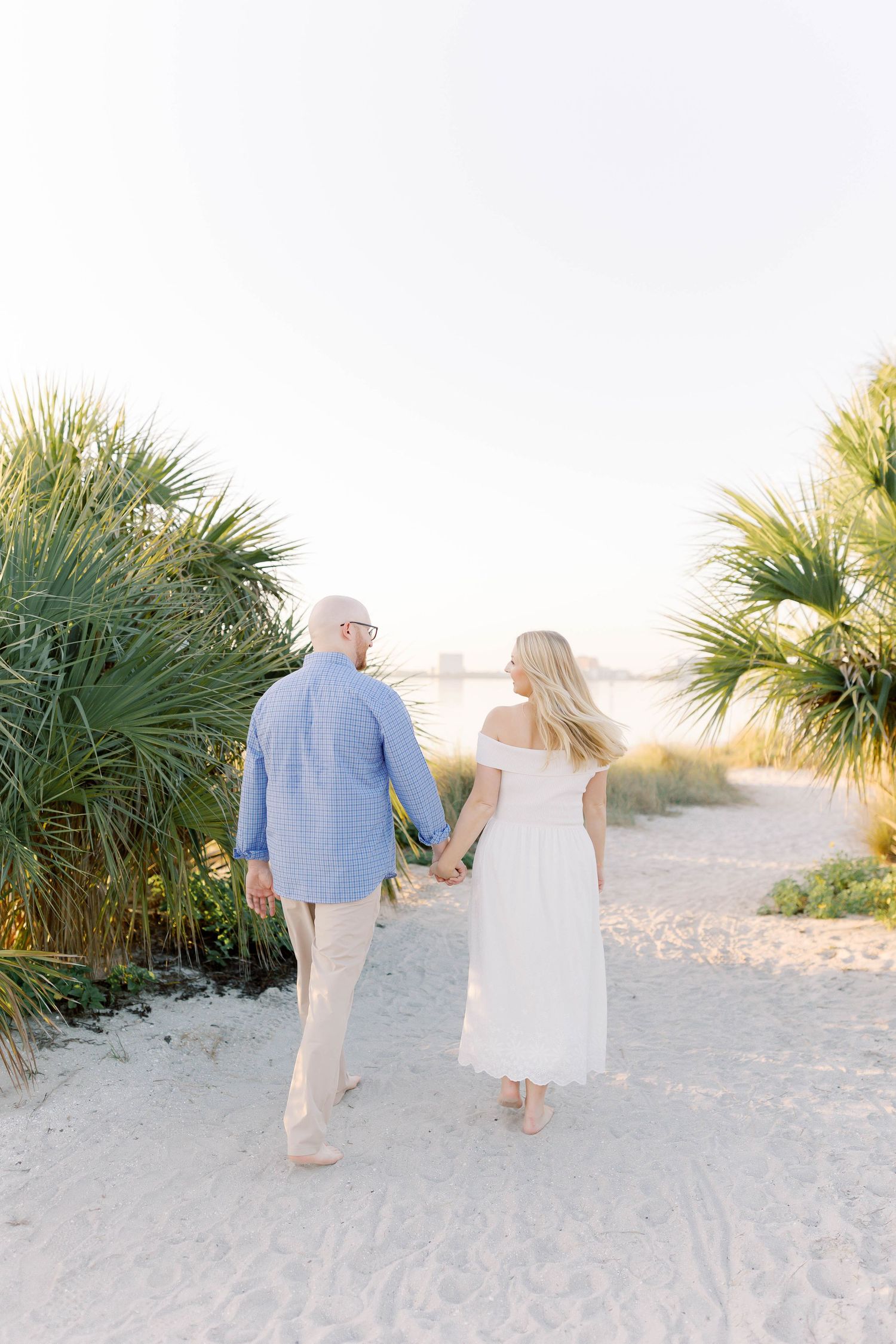 Couple strolling hand in hand past palm trees on white sandy beach.