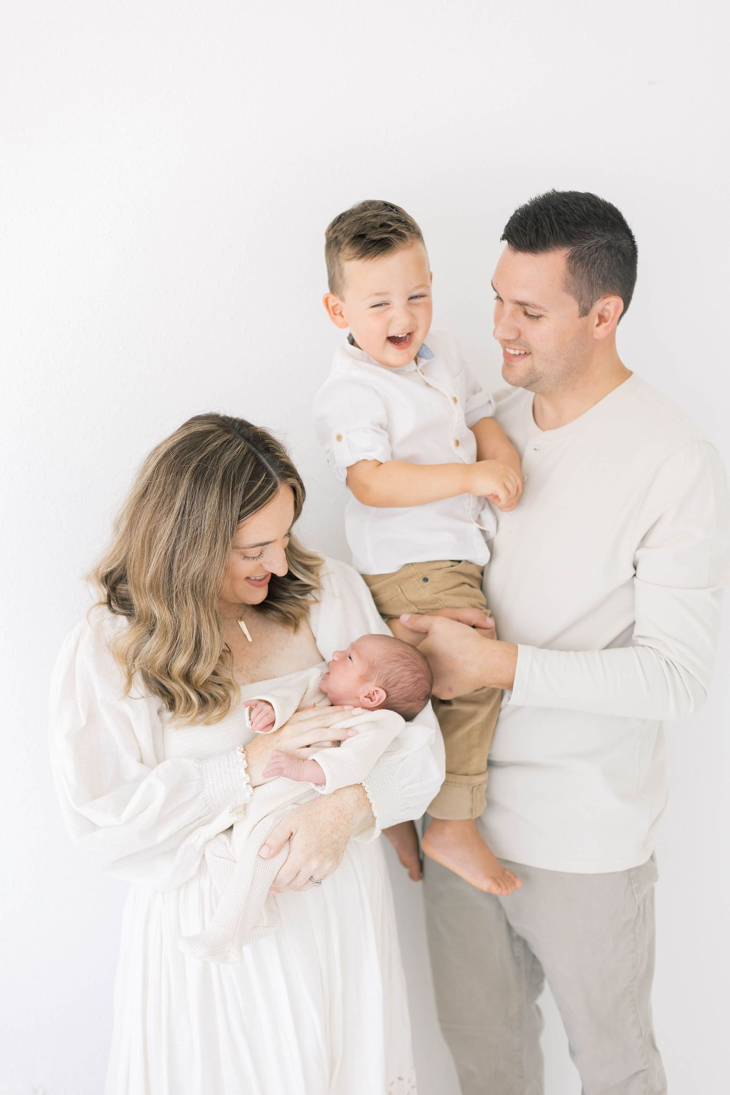 Candid family moments captured in soft white tones showing affection with their children.
