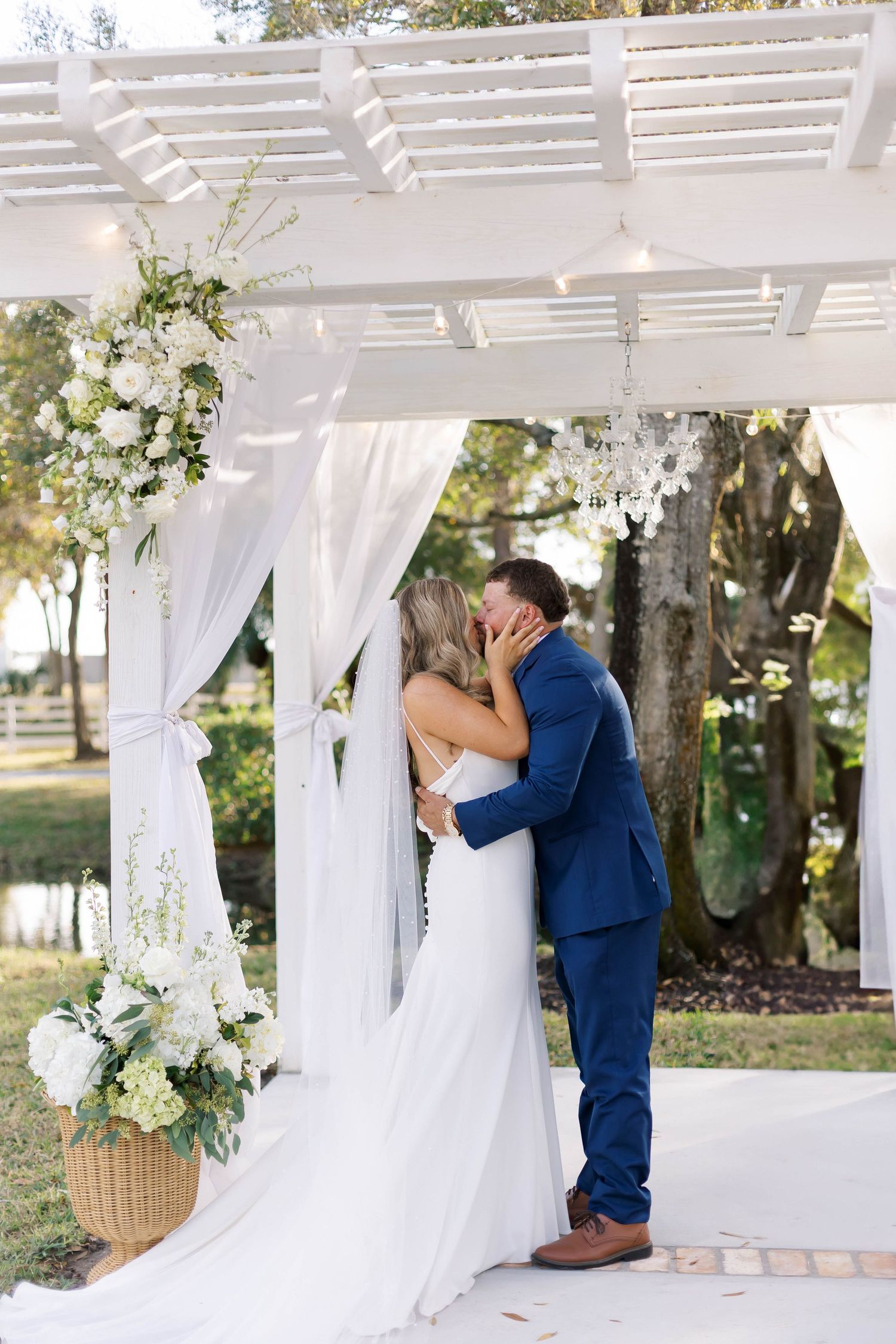 Romantic wedding ceremony moment under a white pergola decorated with flowers.