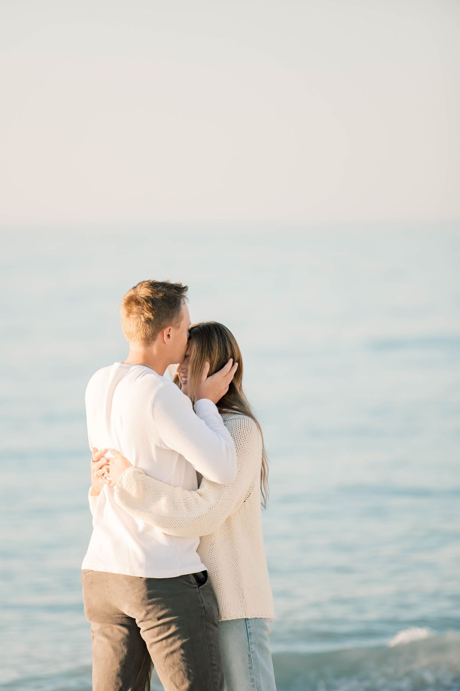 A couple shares a romantic moment on a sunlit beach with soft waves in the background.