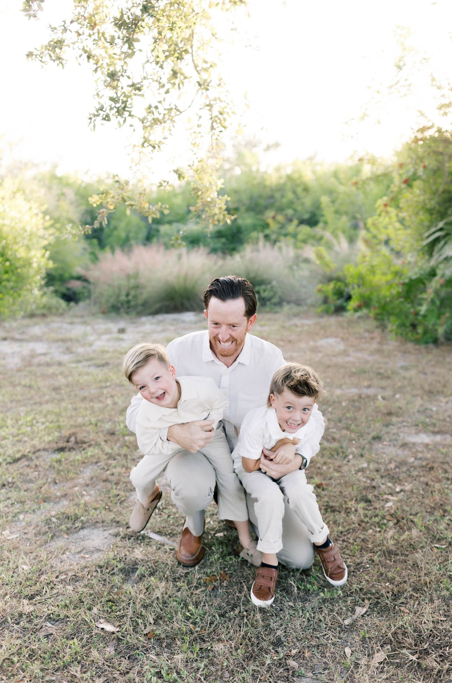 Joyful candid moment of family members laughing together while sitting outdoors in coordinated white outfits.