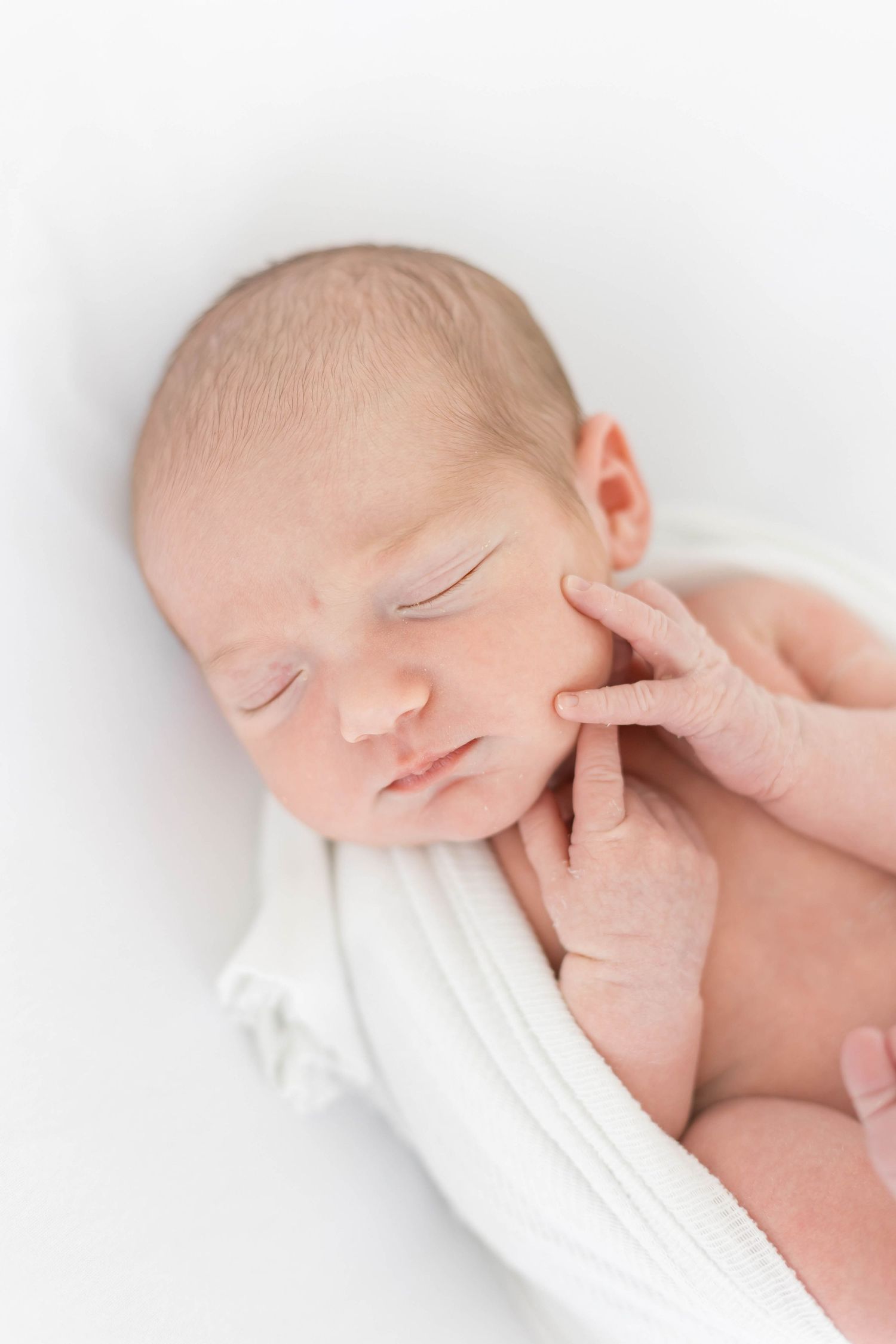 Gentle hand touching sleeping newborn's face against white background.