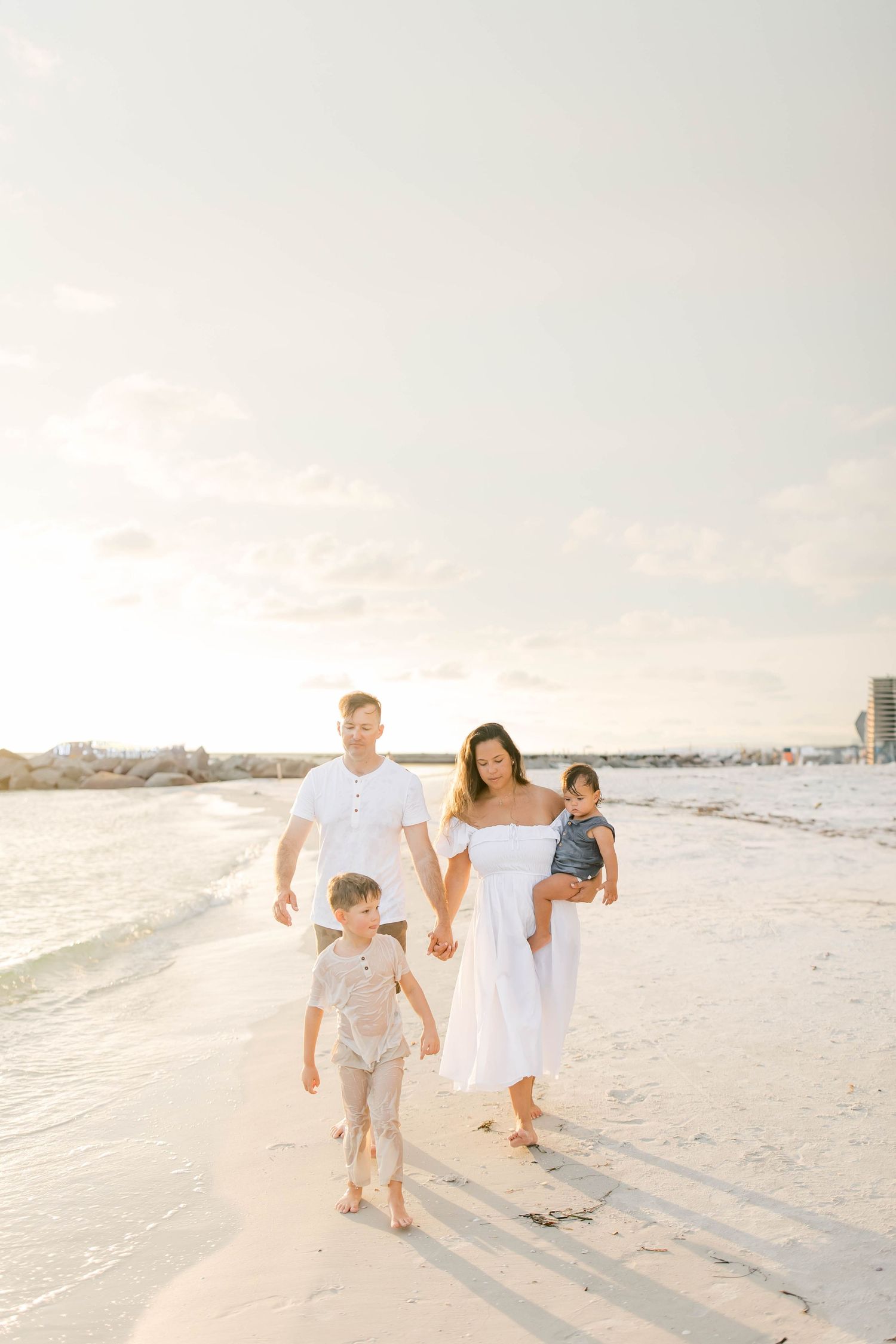 Family walking together along a serene beach at sunset in coordinated white outfits.