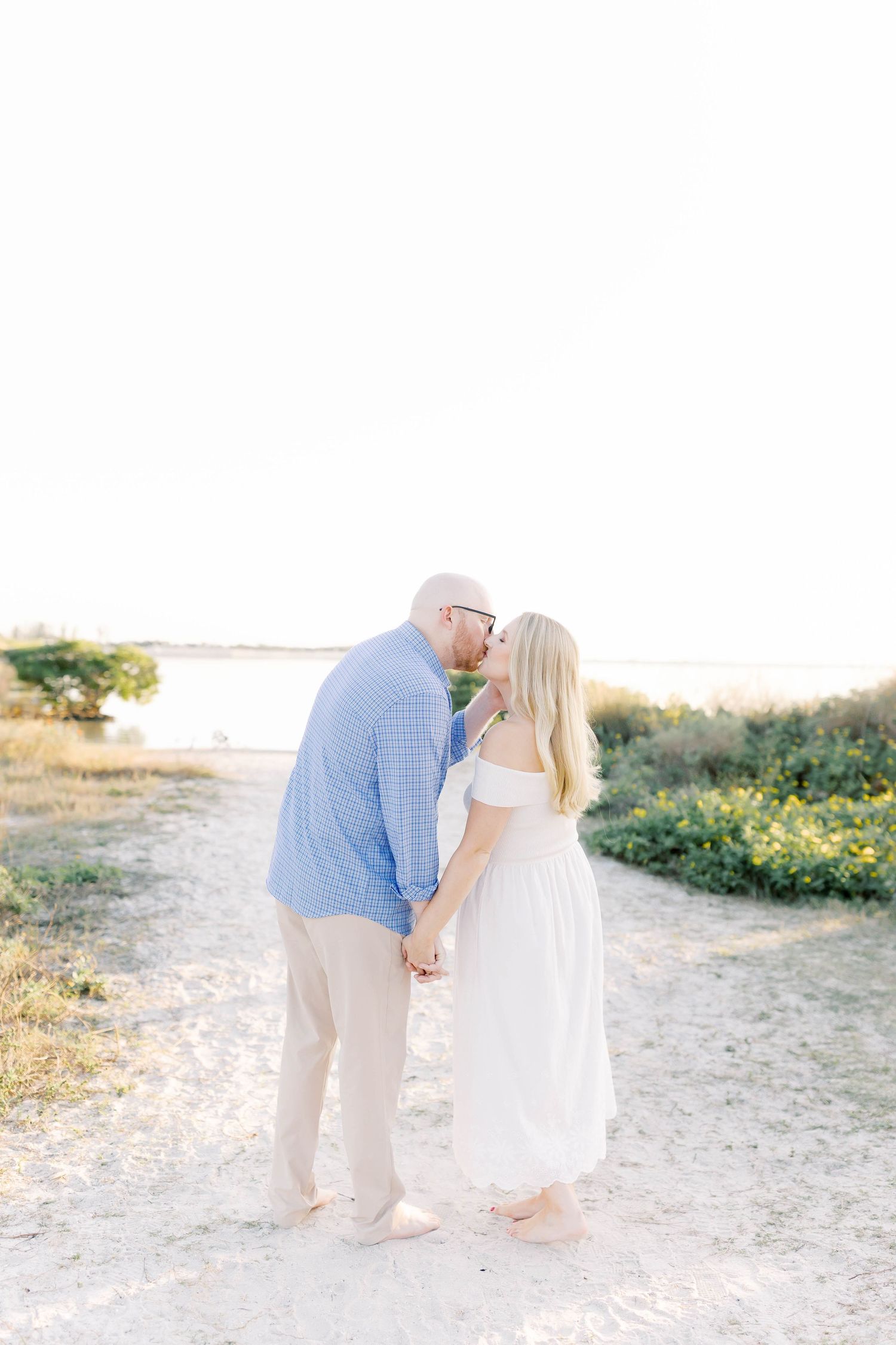 Romantic beach photoshoot with couple in light summer attire against natural backdrop.