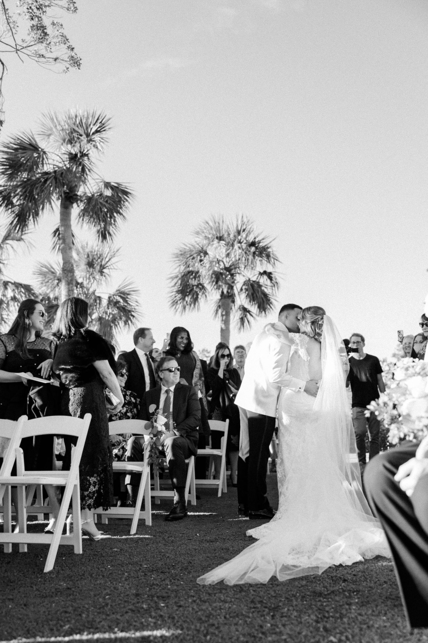 Outdoor wedding ceremony setup with white chairs and palm trees in the background.