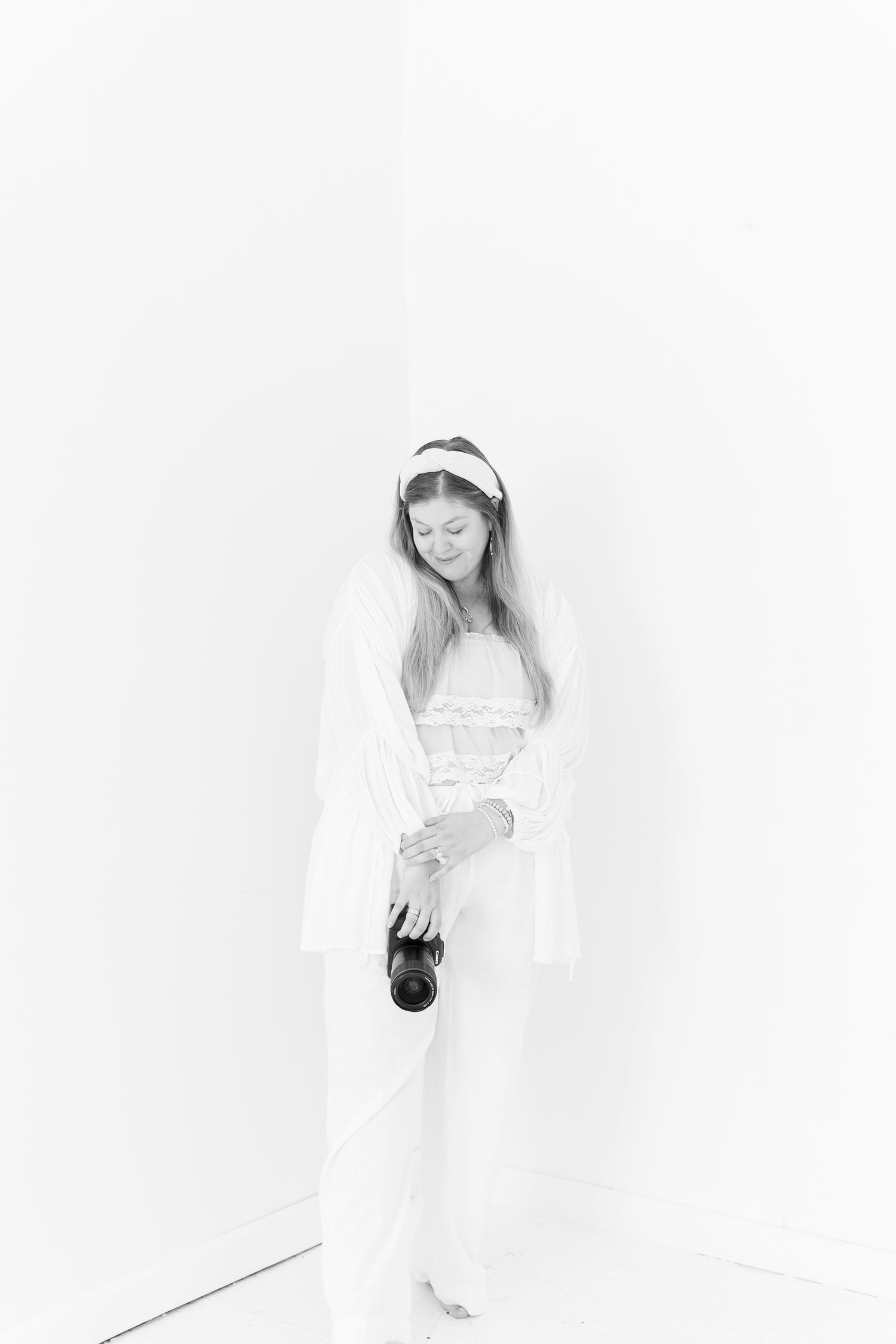 A minimalist black and white portrait showing a person in white holding camera equipment.