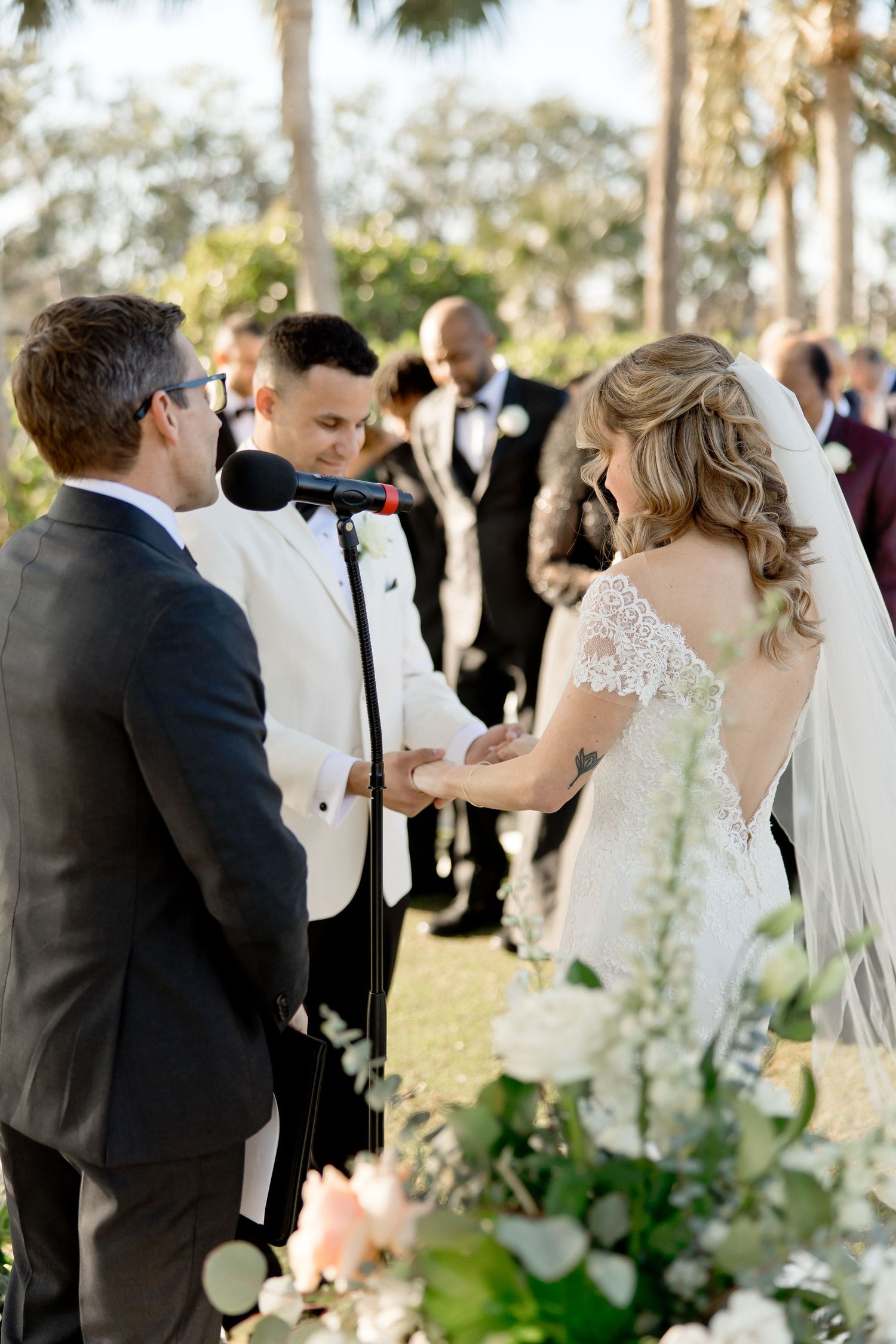 Wedding ceremony guests gather outdoors under palm trees during a sunset celebration.