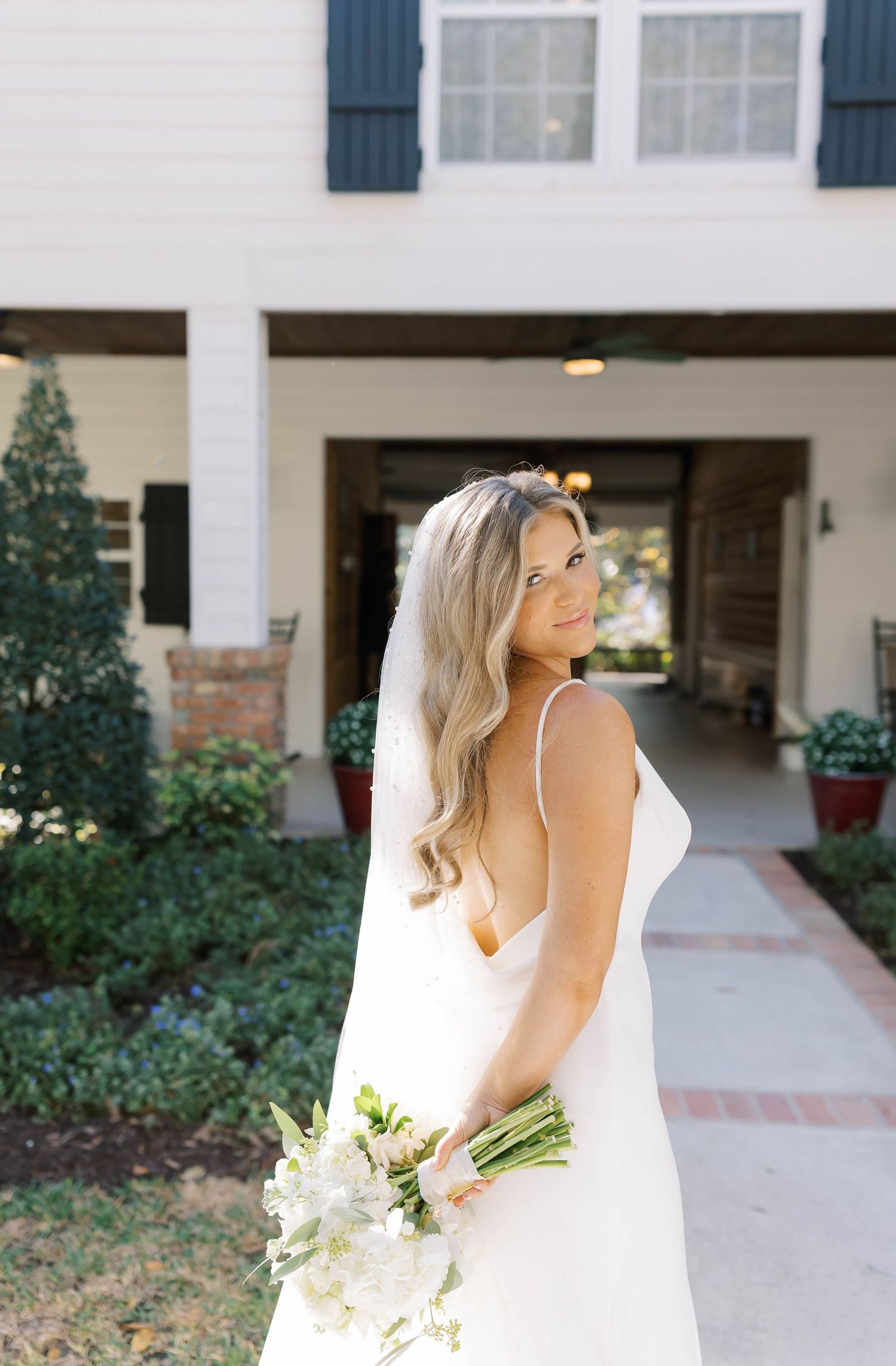 Bride in elegant white dress holds bouquet while posing near venue entrance.