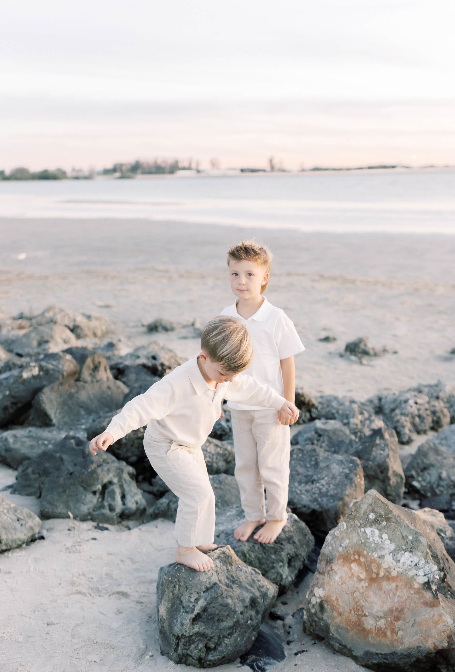 Kids climb on dark rocks at beach while wearing matching white outfits.