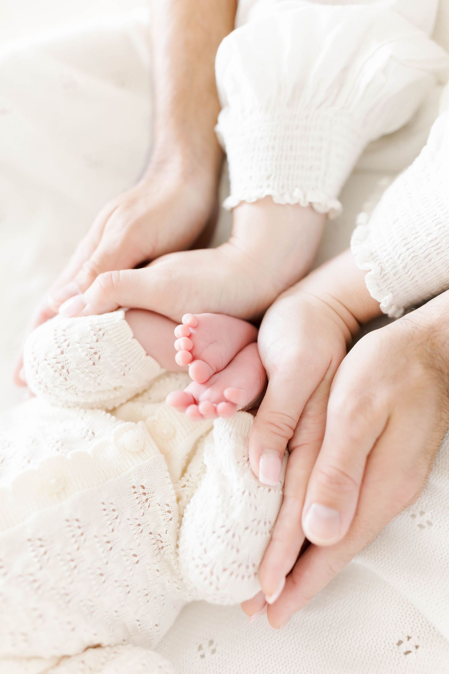 Close-up of tiny baby feet and hands resting on white lace fabric.