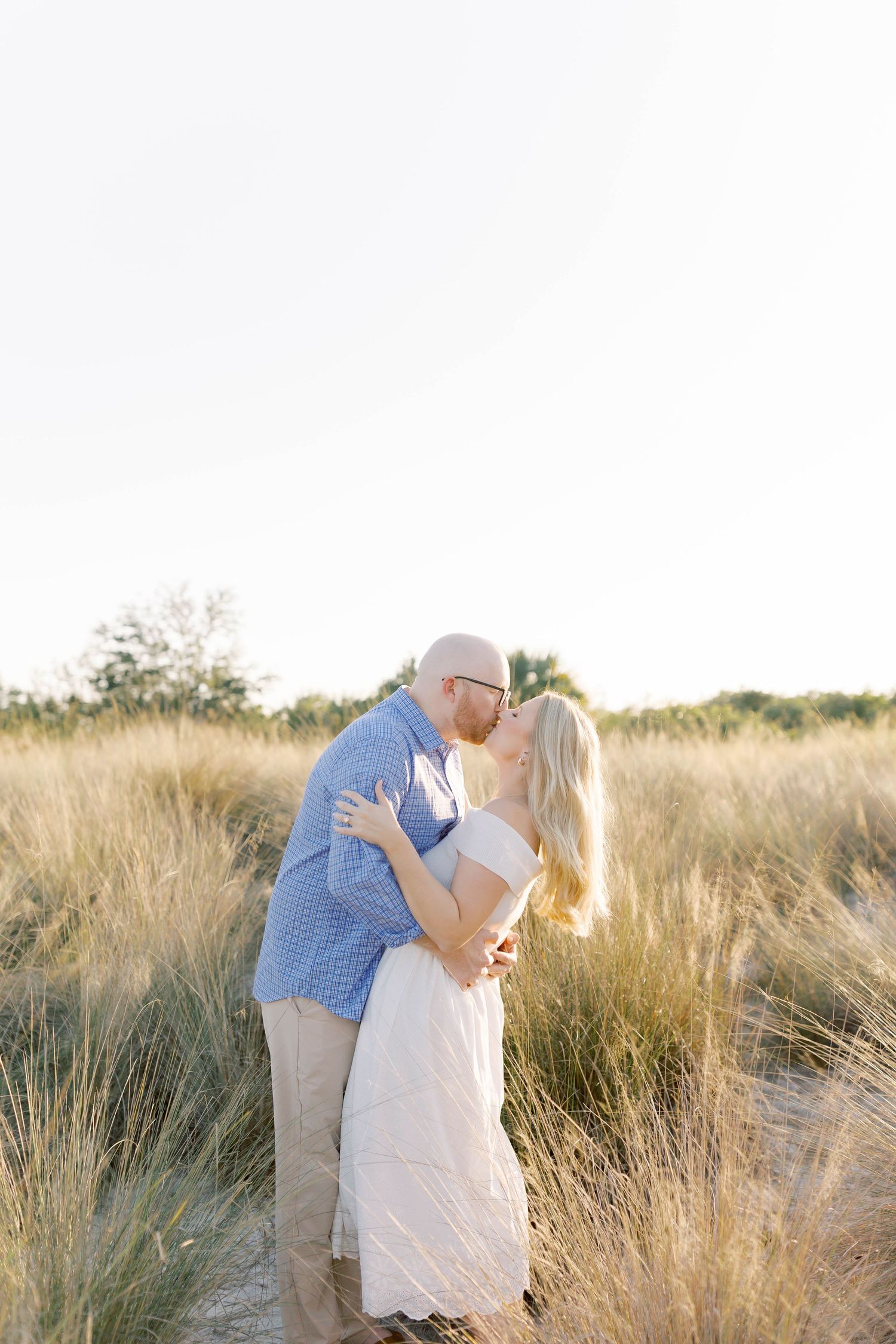 Romantic couple embraces in a sunlit field of tall grass during golden hour.