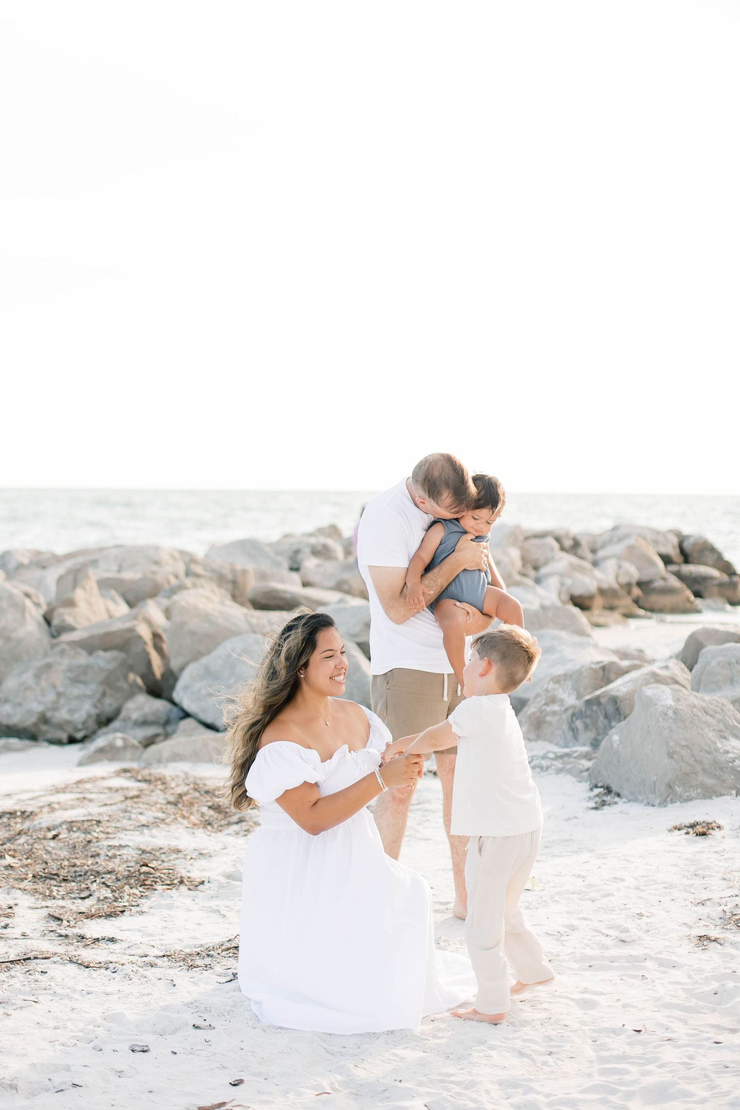 Playful family interactions on a sandy beach with rocky shoreline.
